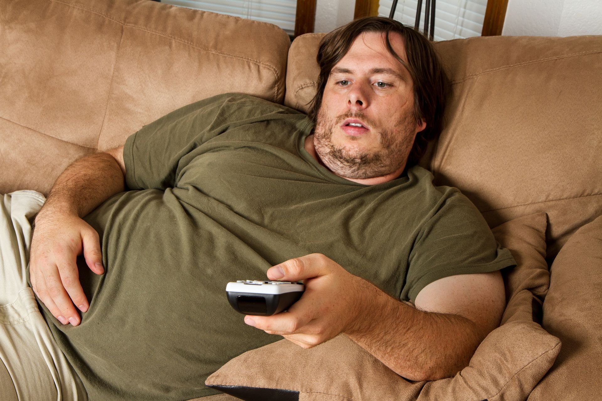 Man reclines on a couch, holding a remote. He wears a green shirt.