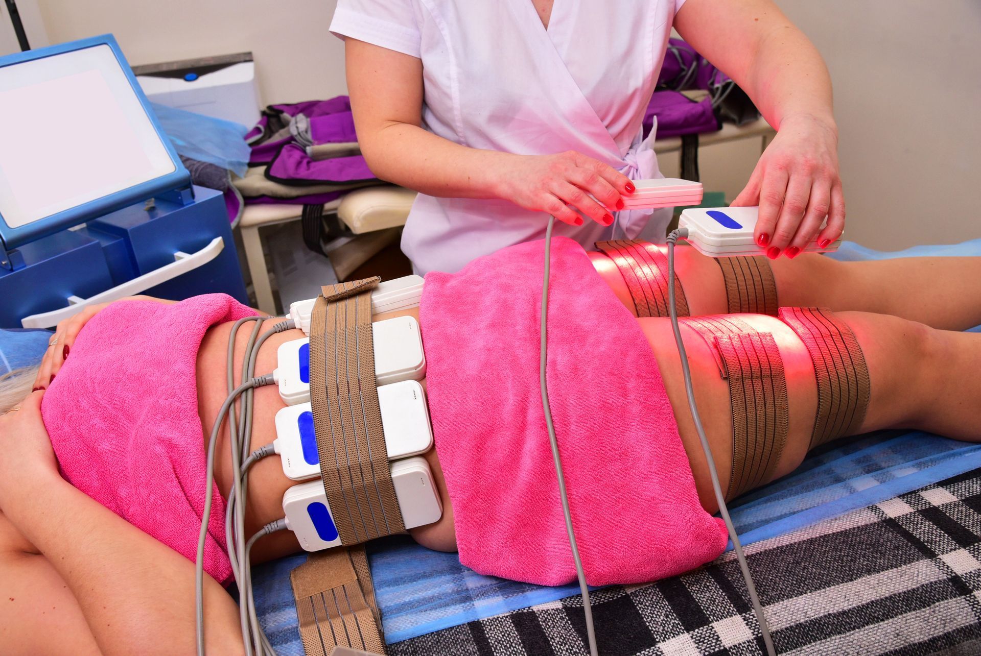Person receiving body contouring treatment with straps and devices. A technician adjusts the device.