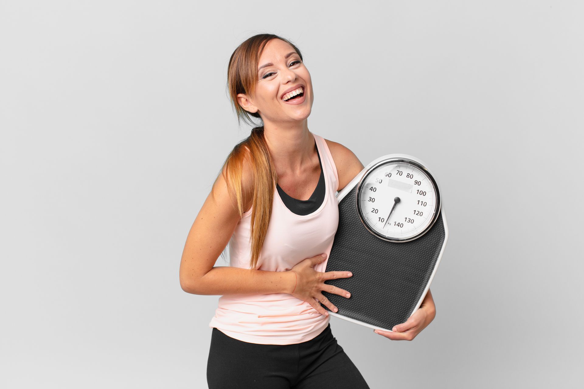 Woman in workout clothes laughing while holding a weight scale.