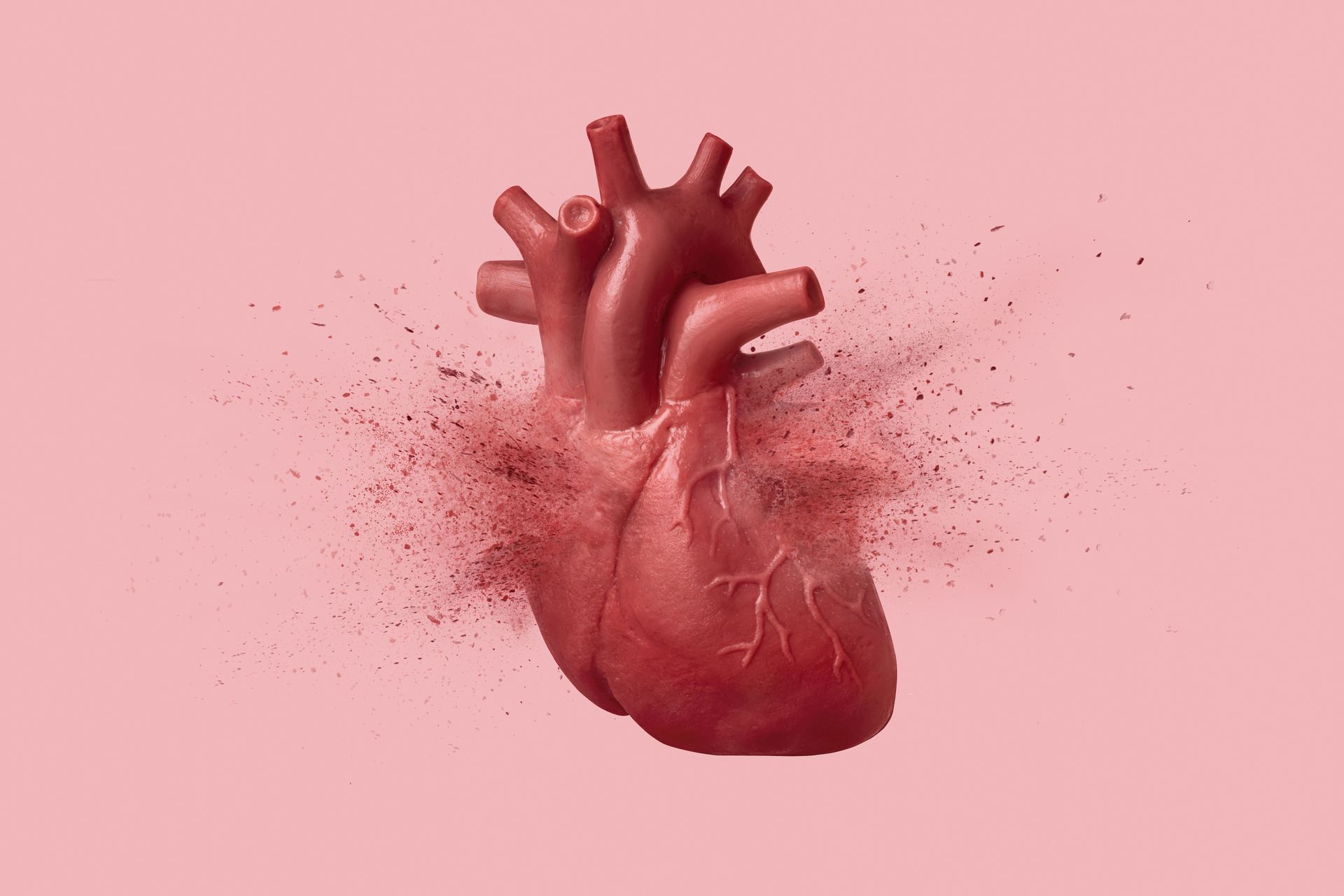 A red human heart exploding into particles against a pink background.