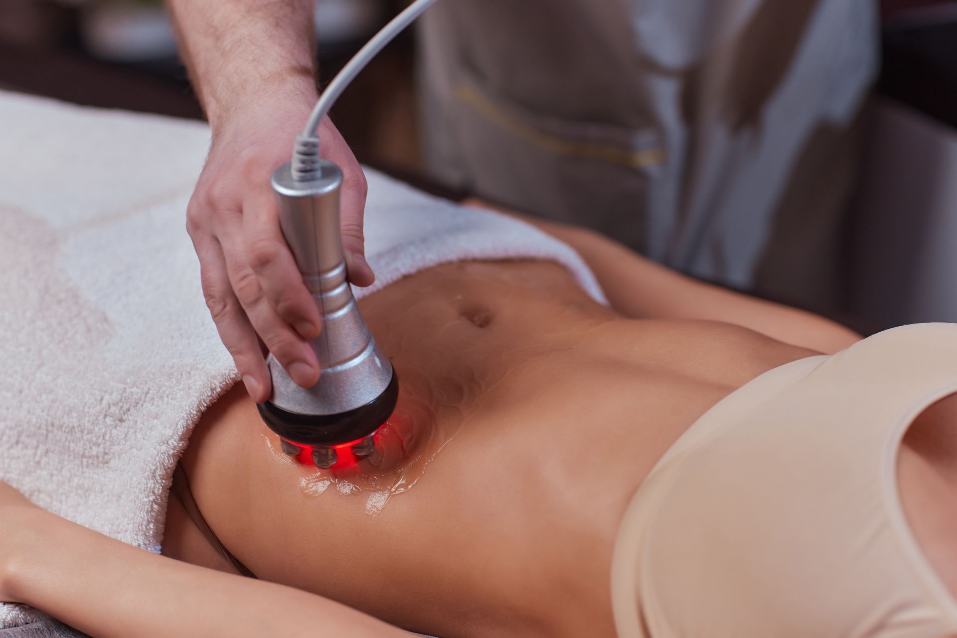 Person receiving body contouring treatment on their abdomen; device with red light is used.