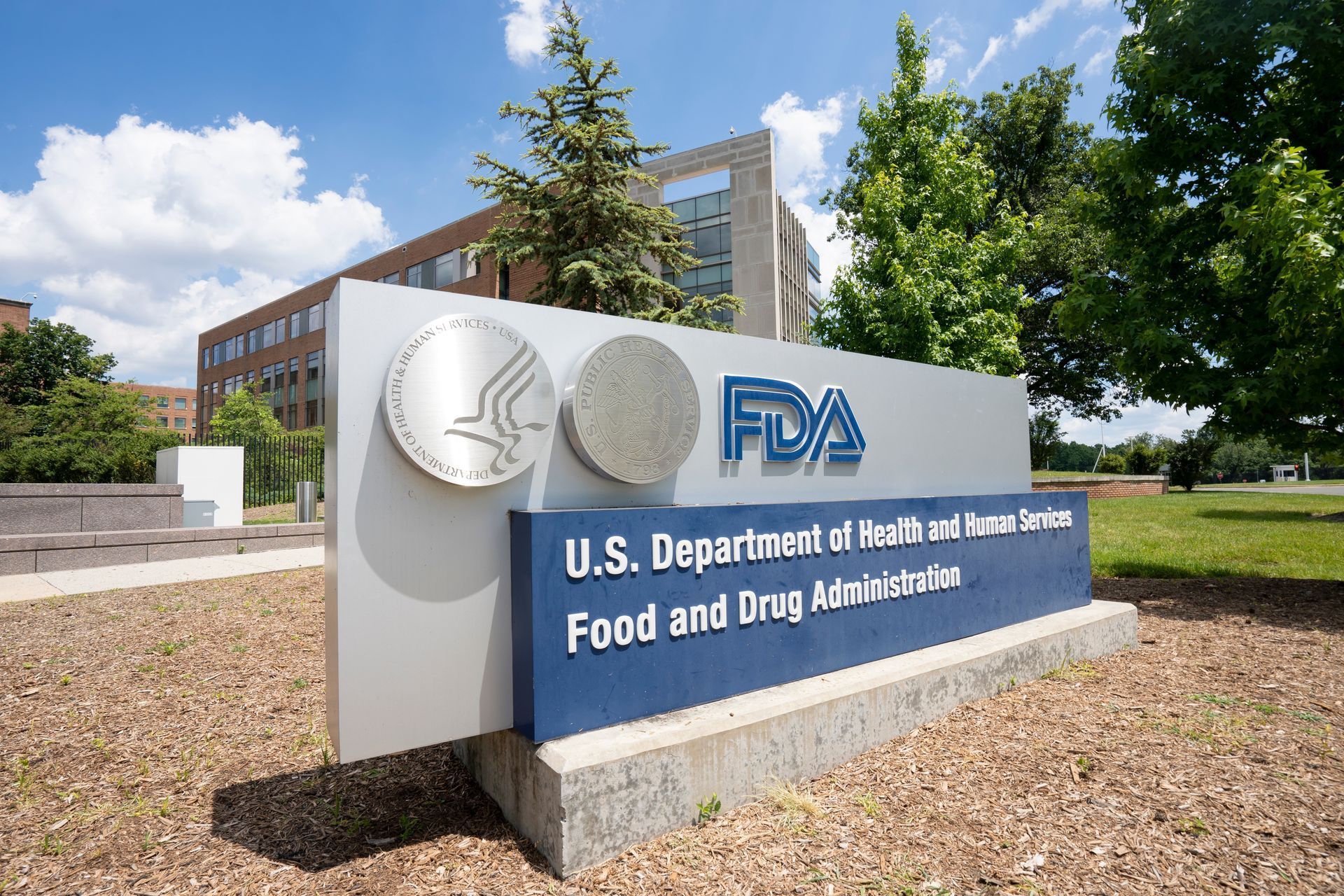 Sign for the U.S. Food and Drug Administration (FDA) with building in background and blue sky.