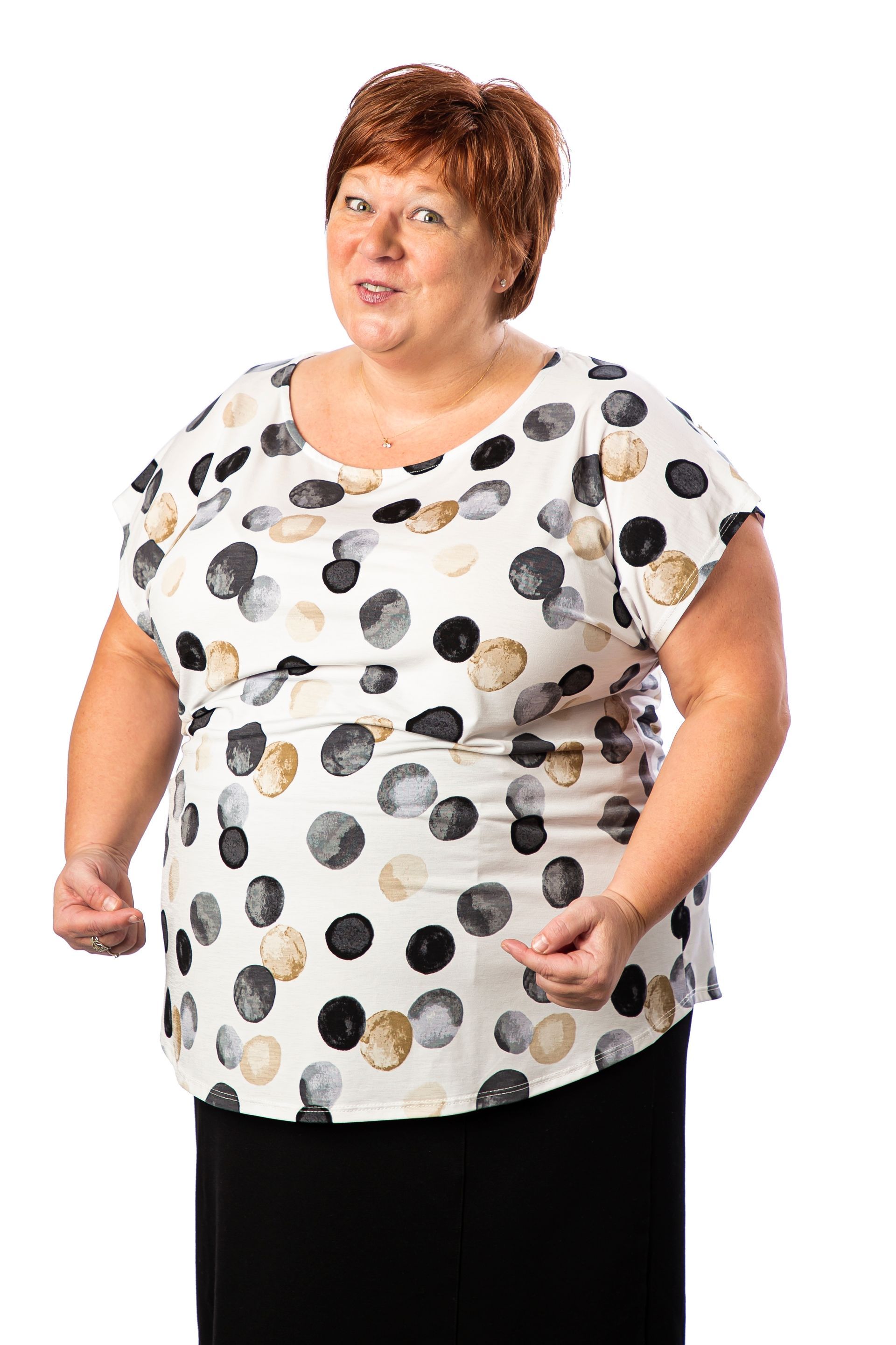 Woman with short red hair wearing a polka-dot top and black skirt, smiling and gesturing with hands.
