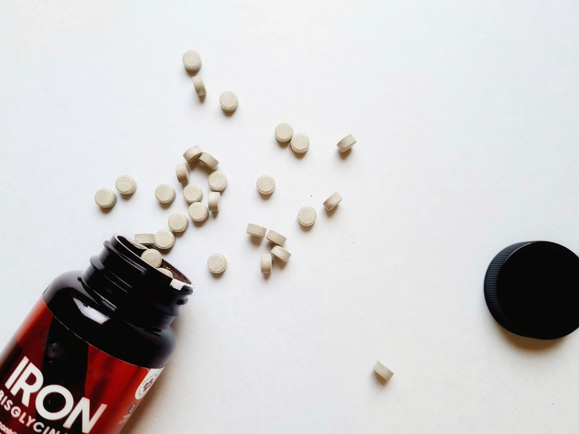 Iron bisglycinate supplement pills spilling from a black bottle on a white surface.