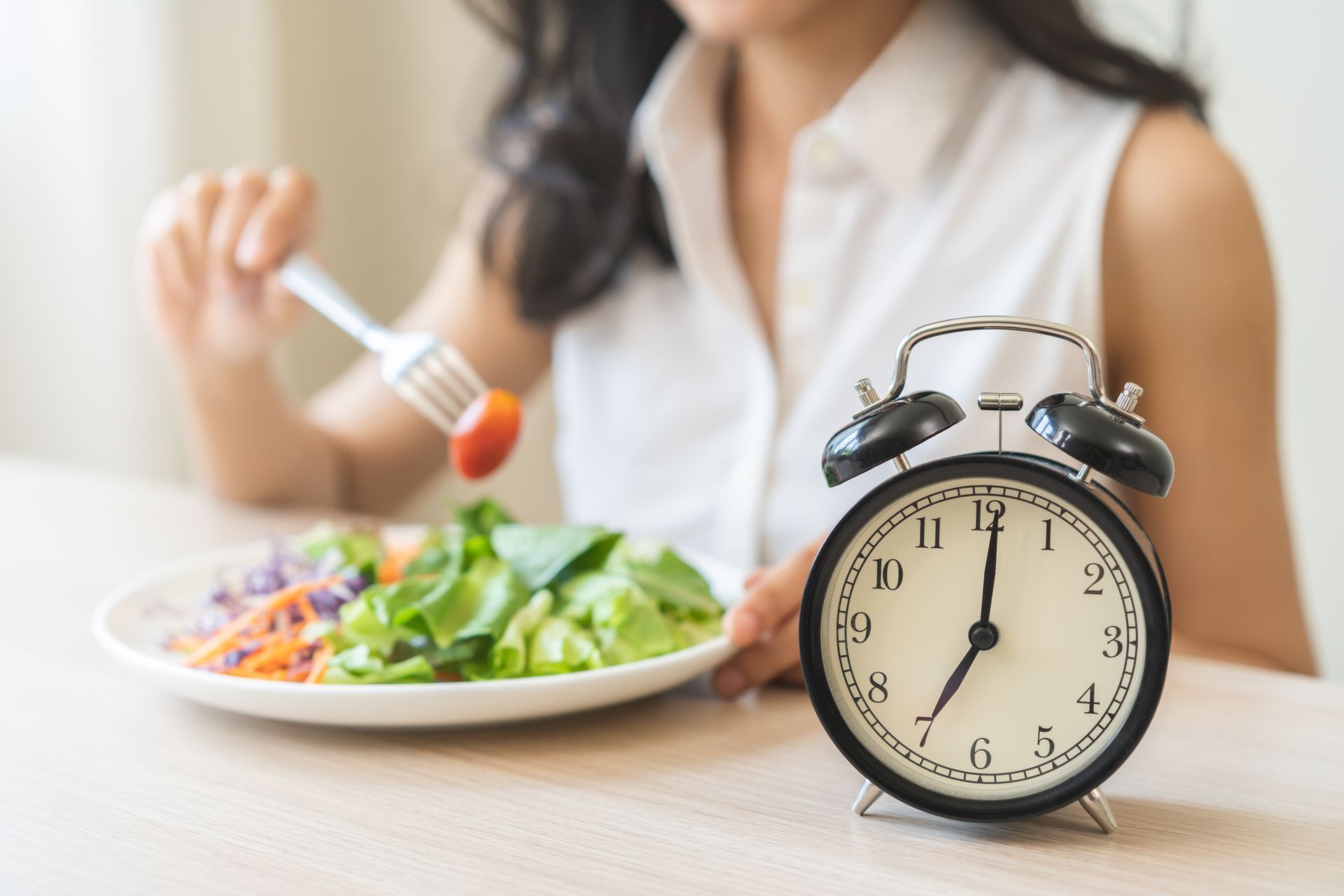 Woman eating salad with a clock at 7:00, implying meal timing.
