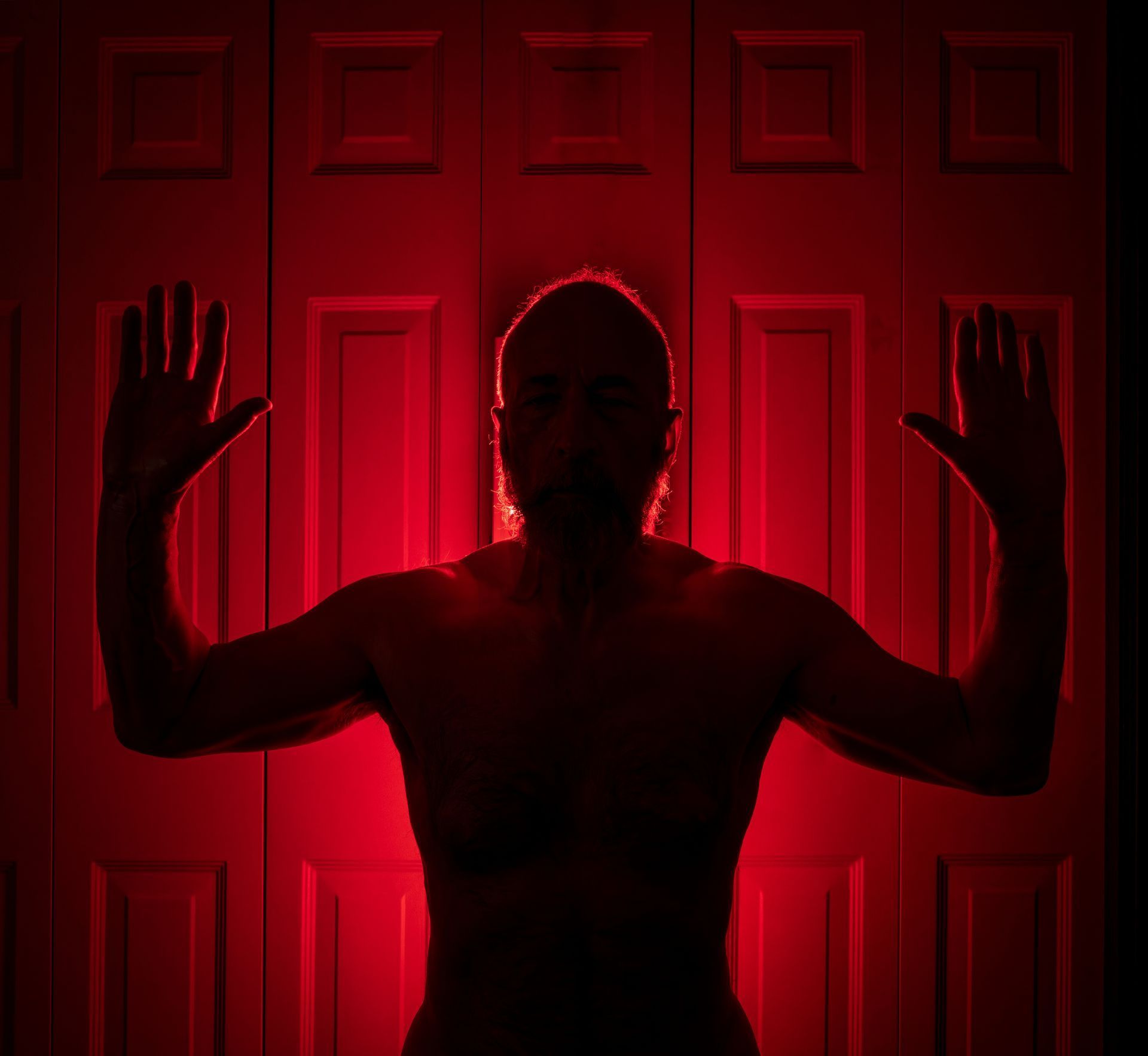 Silhouette of a person with arms raised, illuminated by red light against a closed door.