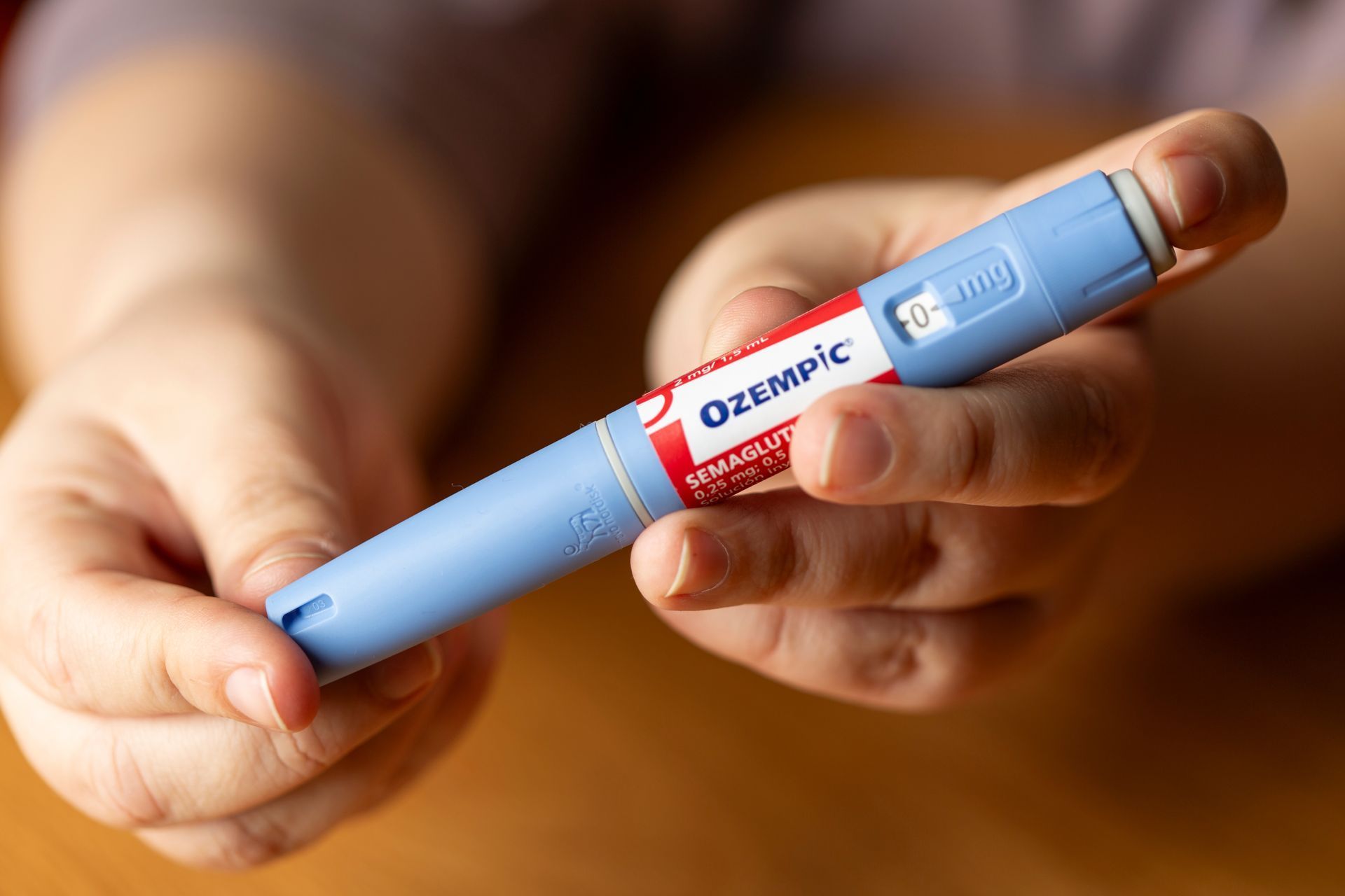 Person holding a light blue Ozempic injection pen with red and white labeling.