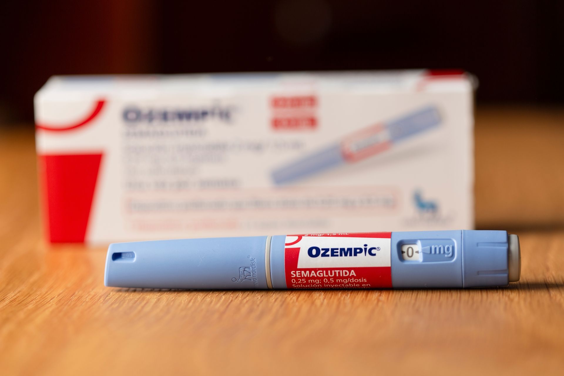 Ozempic injection pen with its box on a wood surface. Blue pen with red label.