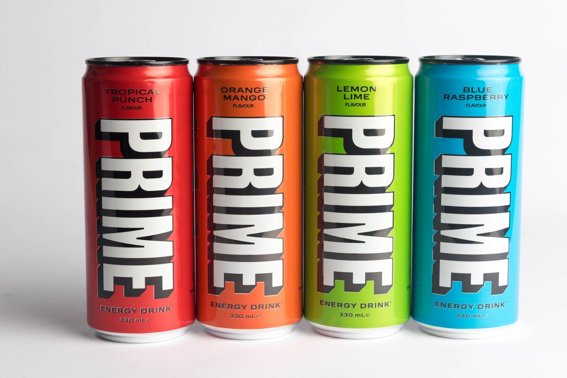 Four cans of PRIME energy drink in red, orange, green, and blue, labeled with the brand name.