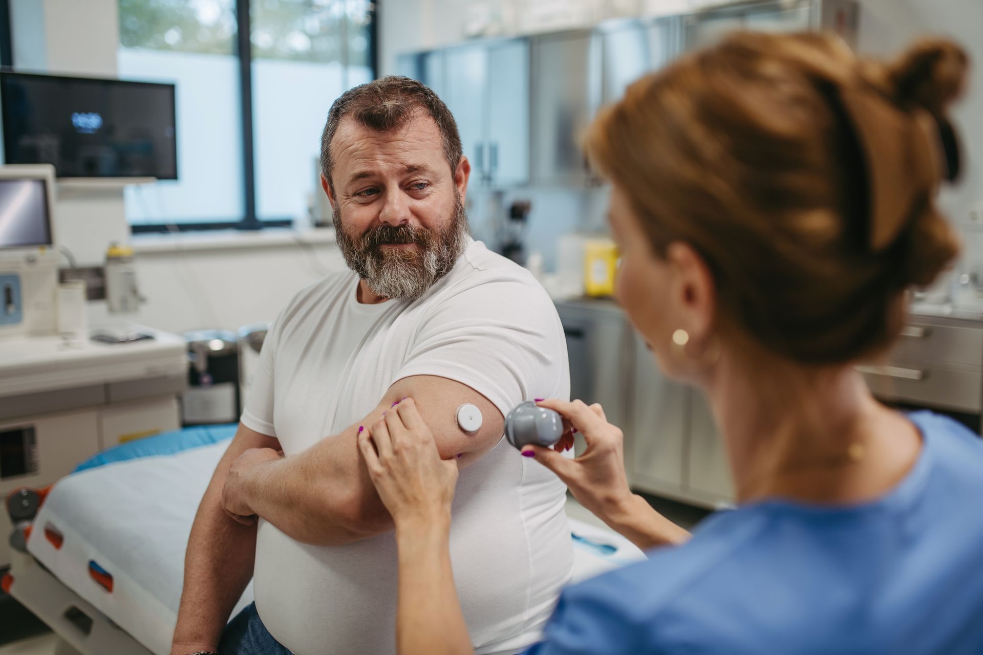 A healthcare worker places a medical device on a patient's arm in a medical setting.