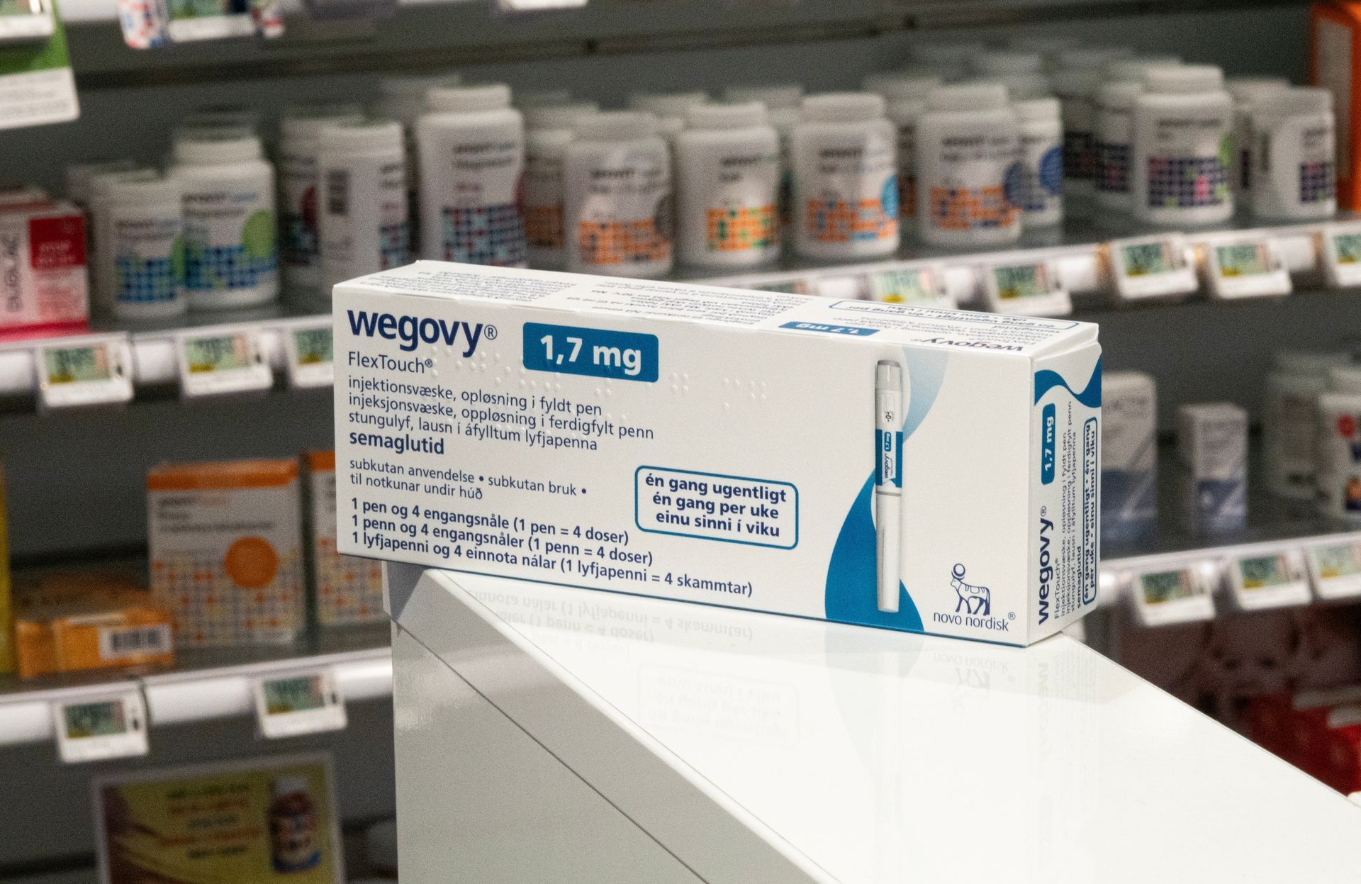 Box of Wegovy 1.7 mg medication on a shelf in a pharmacy, surrounded by other products.