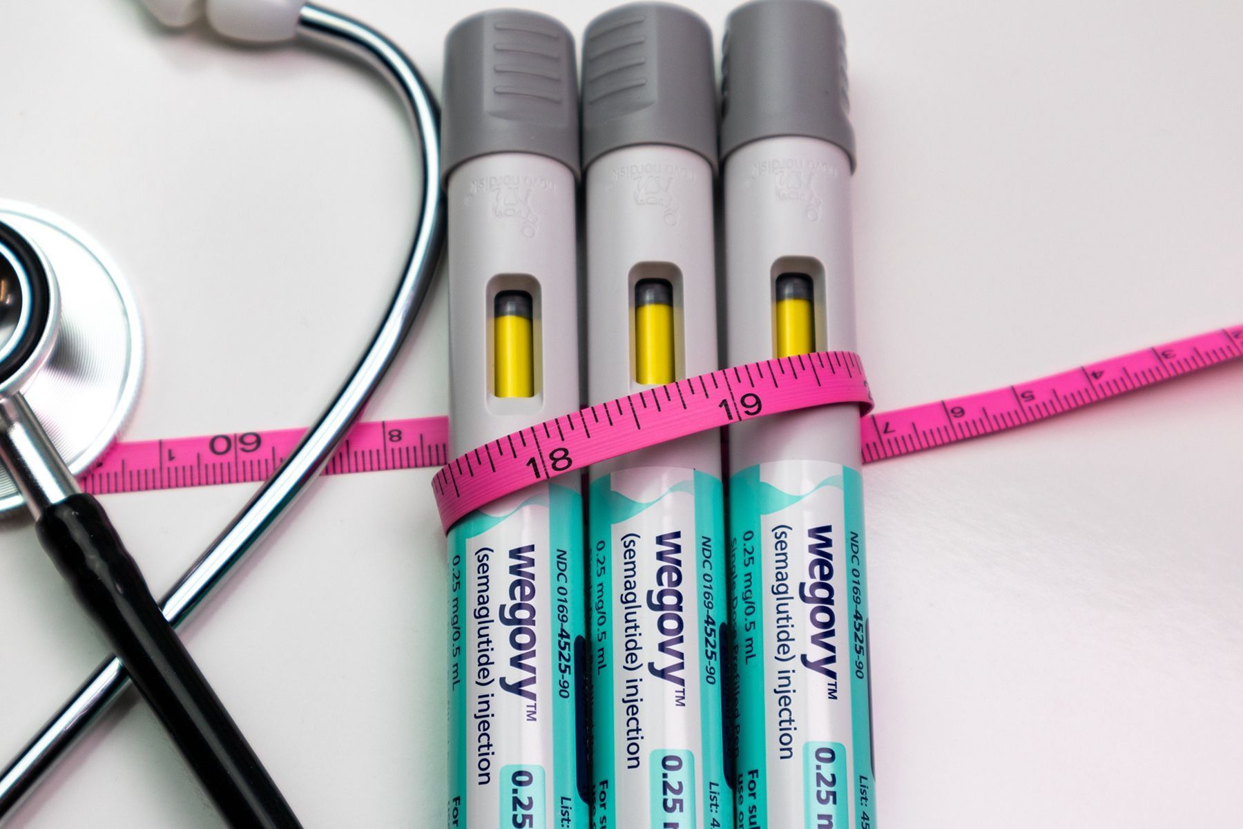 Three Wegovy pens with measuring tape and stethoscope on a white surface.