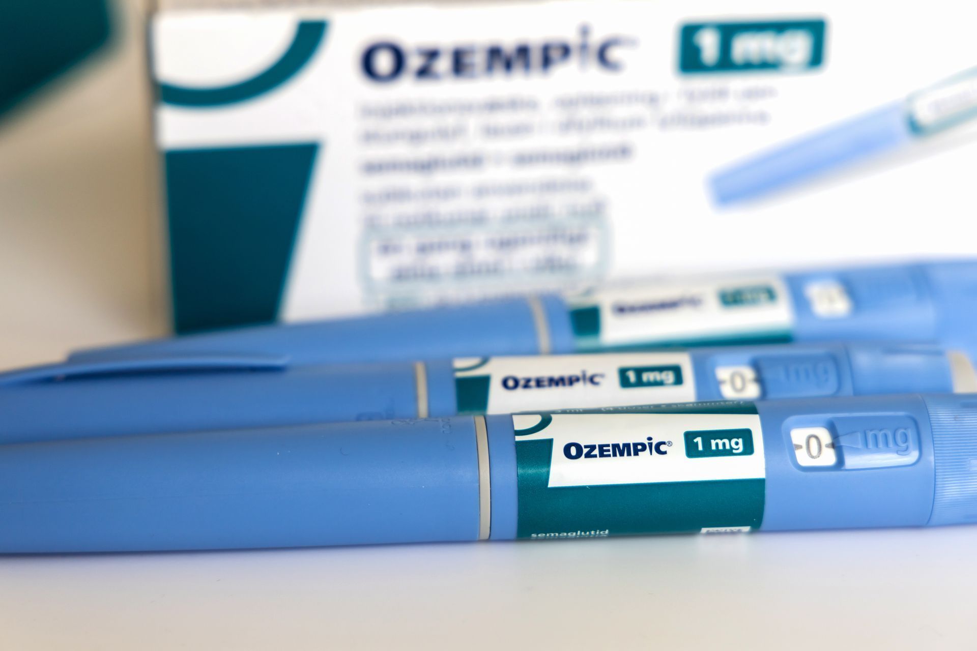 Ozempic 1 mg injection pens and box in focus, light blue with green label.