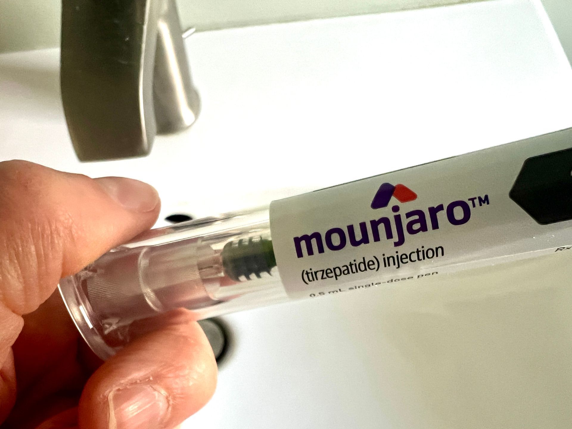Person holding Mounjaro pen near a sink; medication for injection.