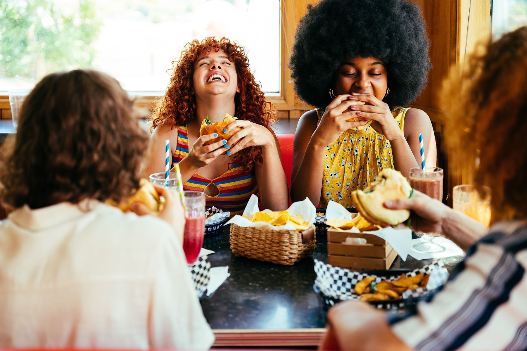 Four people eating burgers and fries, laughing together at a diner booth.
