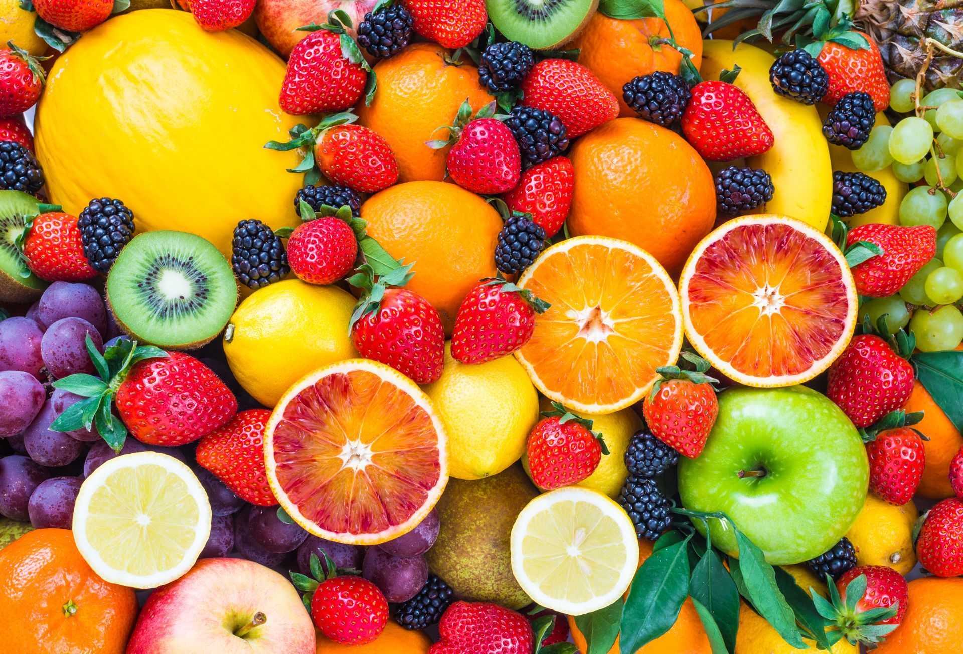 Colorful assortment of fruits, including oranges, strawberries, grapes, and kiwi, arranged closely together.