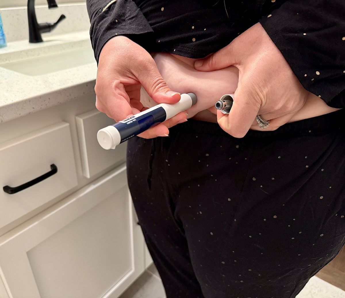 Person injecting medication into abdomen with pen injector in bathroom.