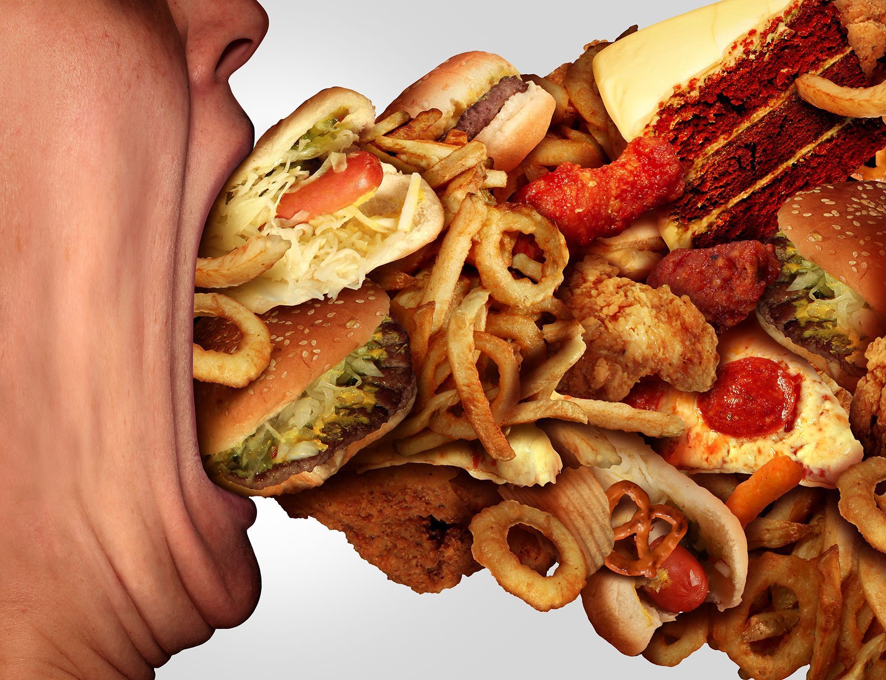 A person’s mouth overflowing with an assortment of unhealthy fast food items.
