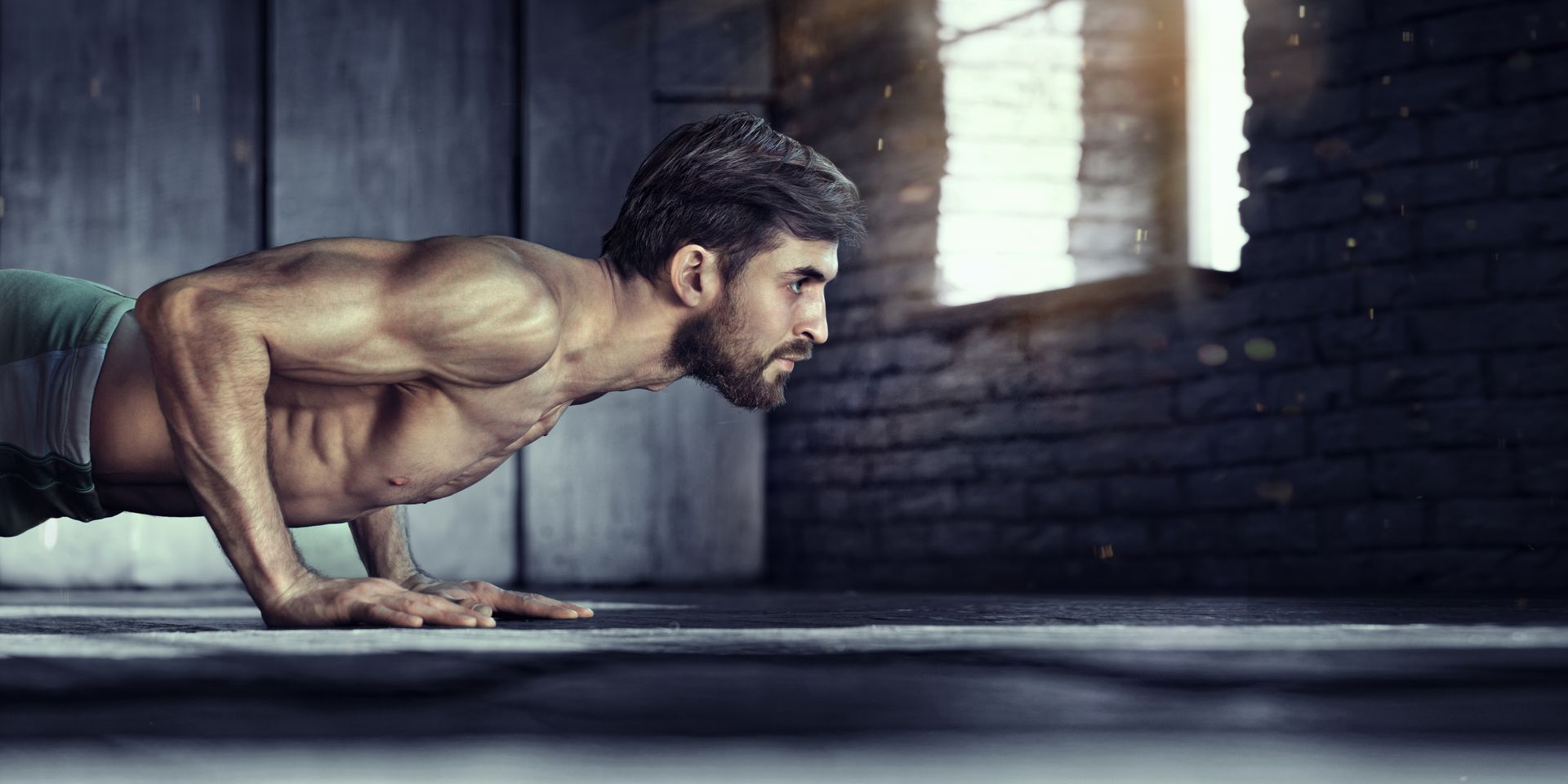 A man doing push-ups in a dimly lit, brick-walled space. He is shirtless.