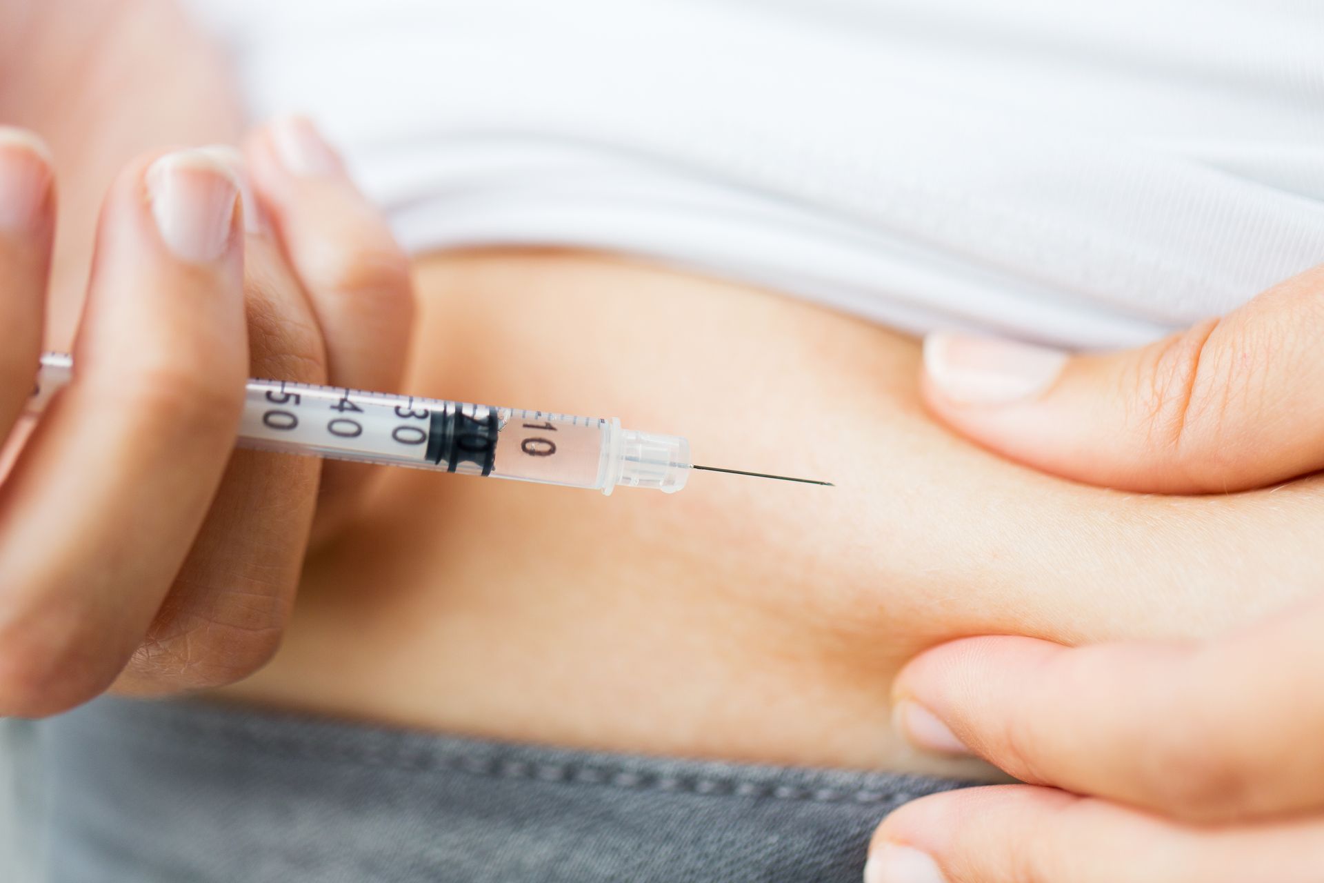 Person injecting themselves with a syringe into the abdomen.