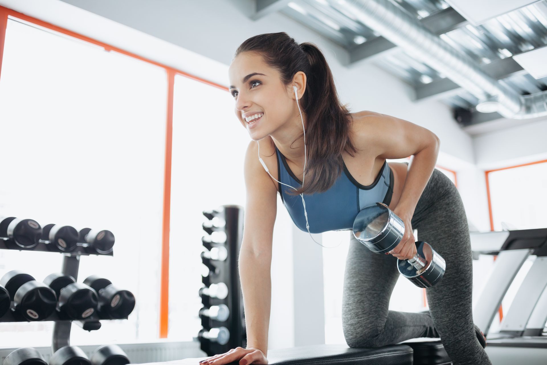Woman exercising with a dumbbell in a gym. She is smiling while lifting weights.