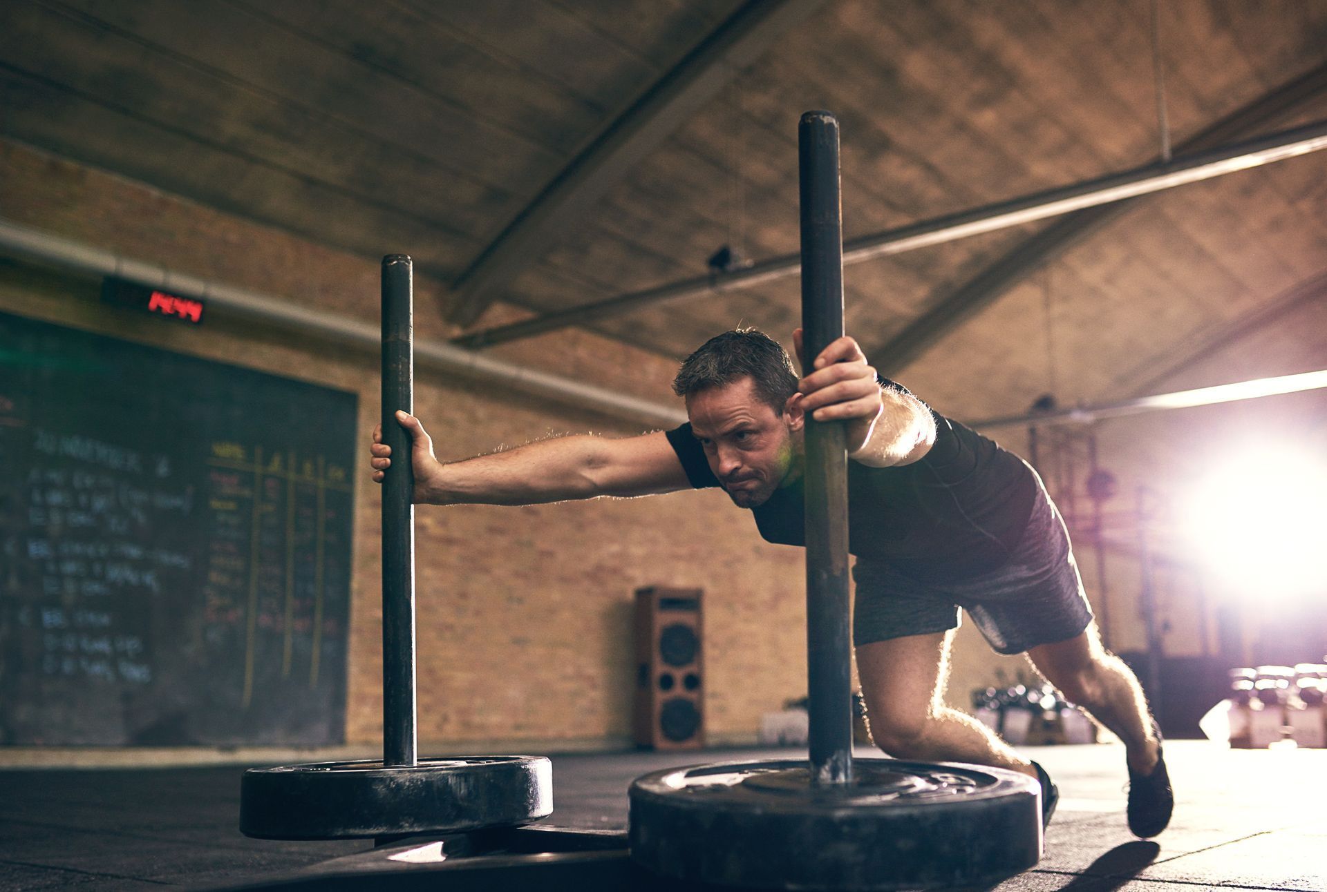 Man pushing weighted sled in a gym; dark clothing, determined expression.