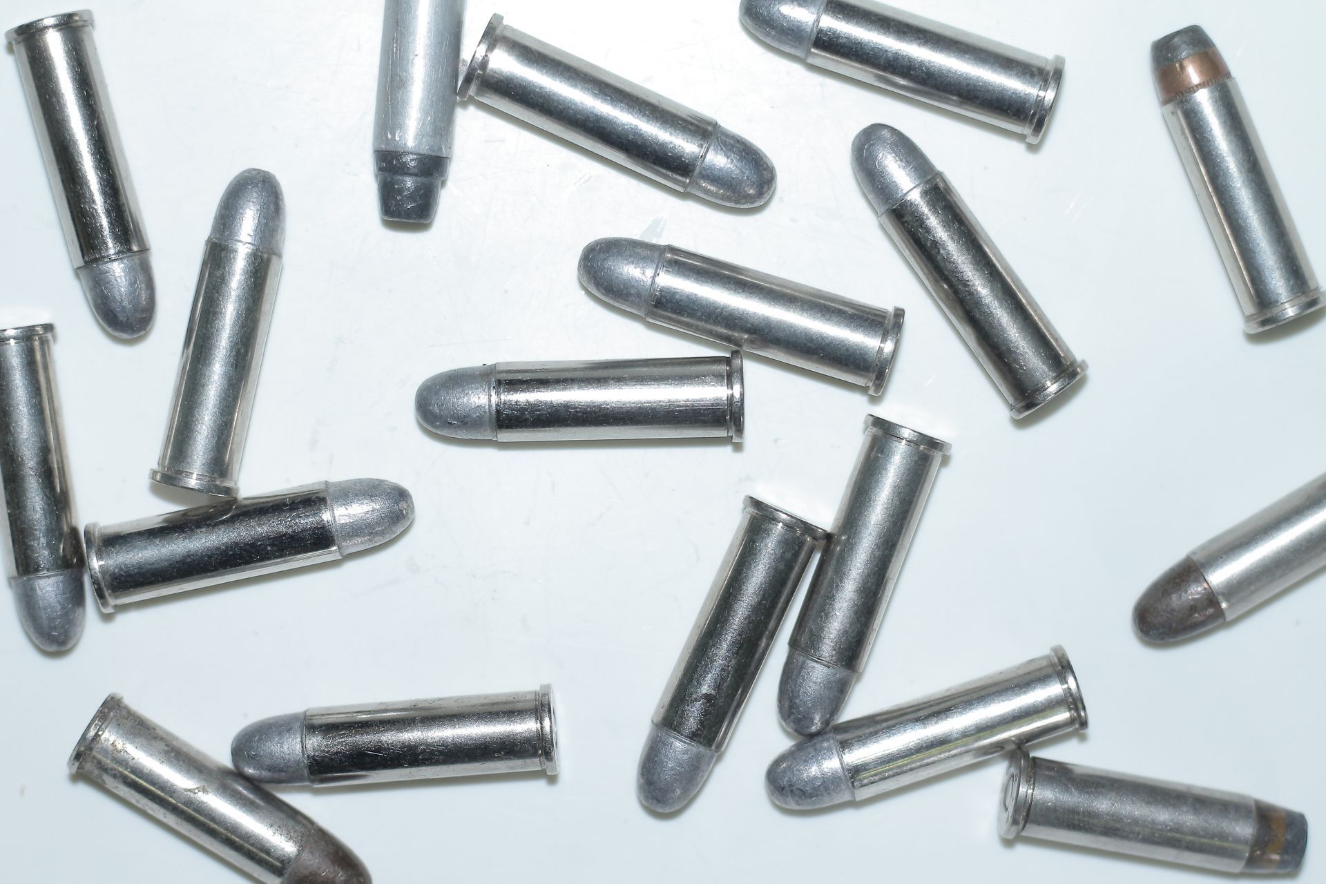 Scattered .22 caliber bullets with silver casings and gray tips on a white surface.