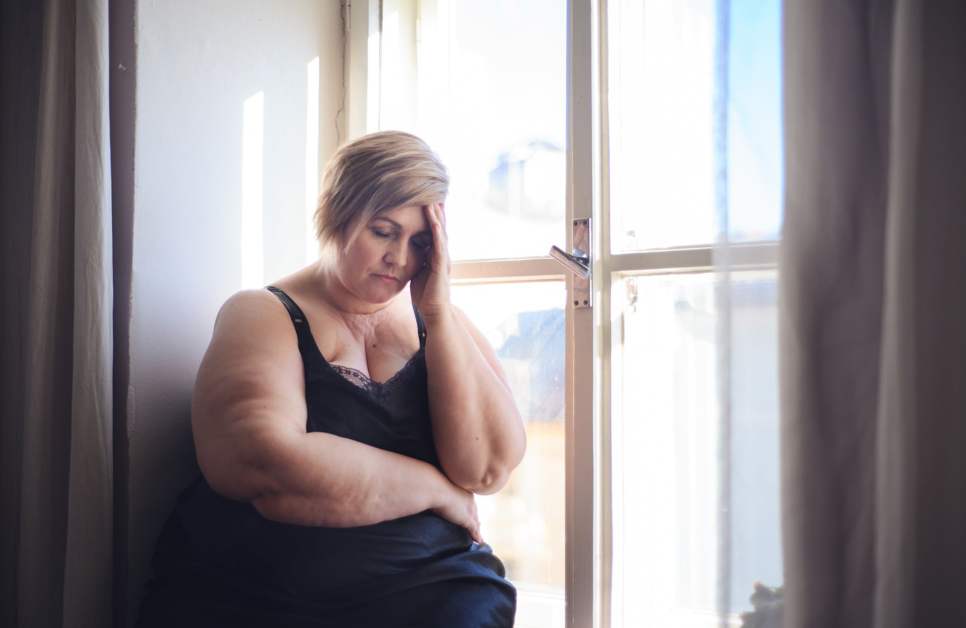 Person sitting by a window, leaning on a hand with a pensive expression.