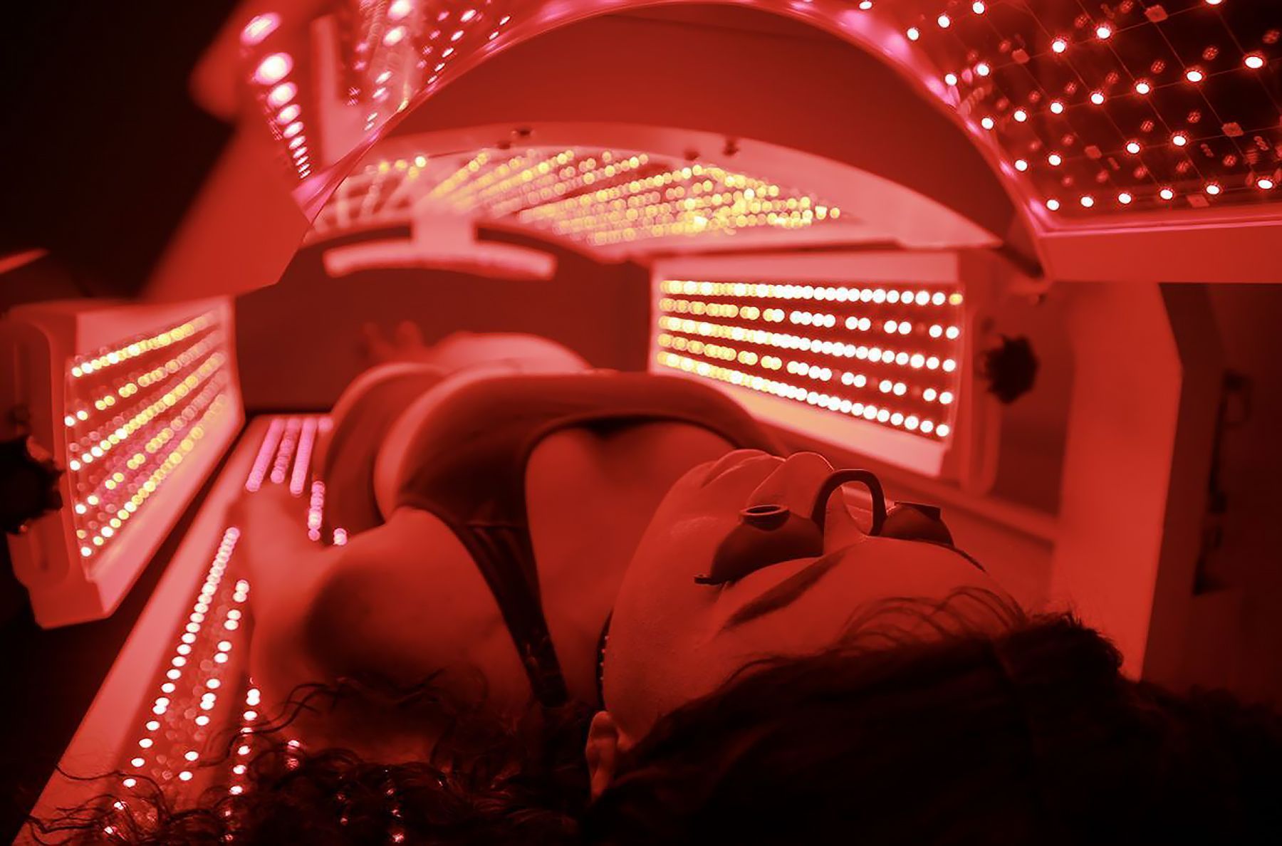 Woman wearing protective glasses lies in a red light therapy bed.