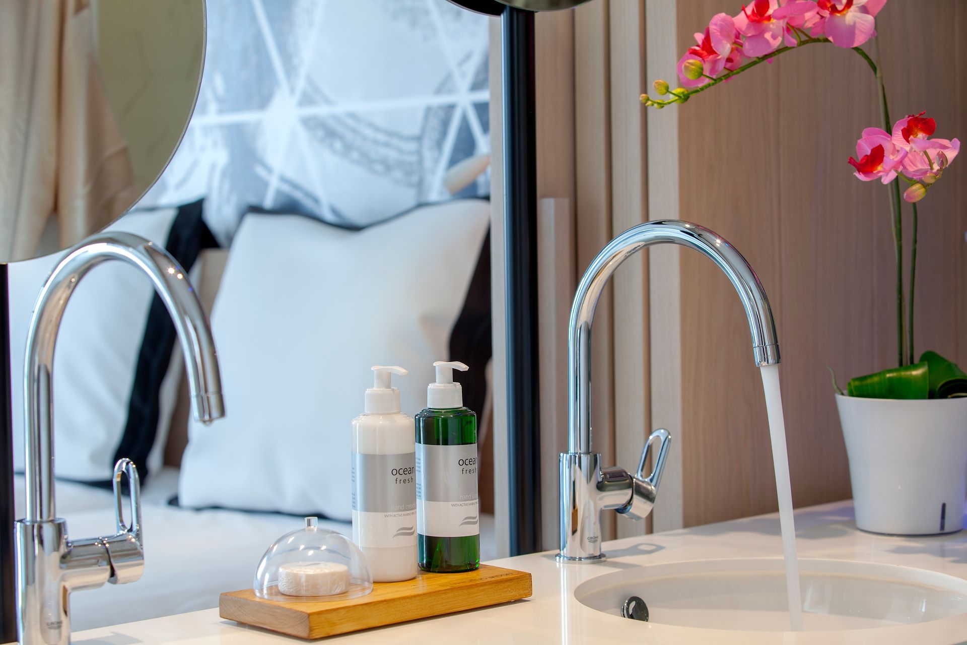 Bathroom sink with running water, soap bottles, a wooden tray, and pink orchids at King Jason Protaras.