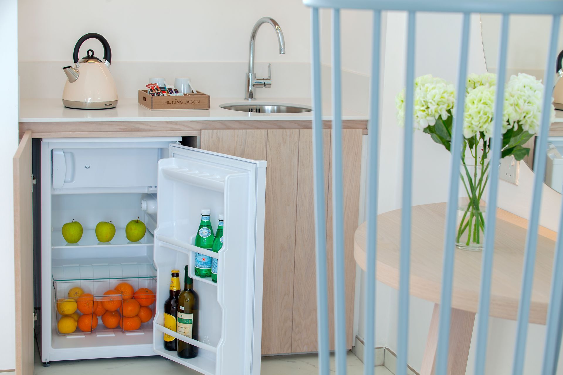 Mini-fridge with fruit and drinks in a small kitchen area. White cabinets, sink, and kettle visible at King Jason Protaras.
