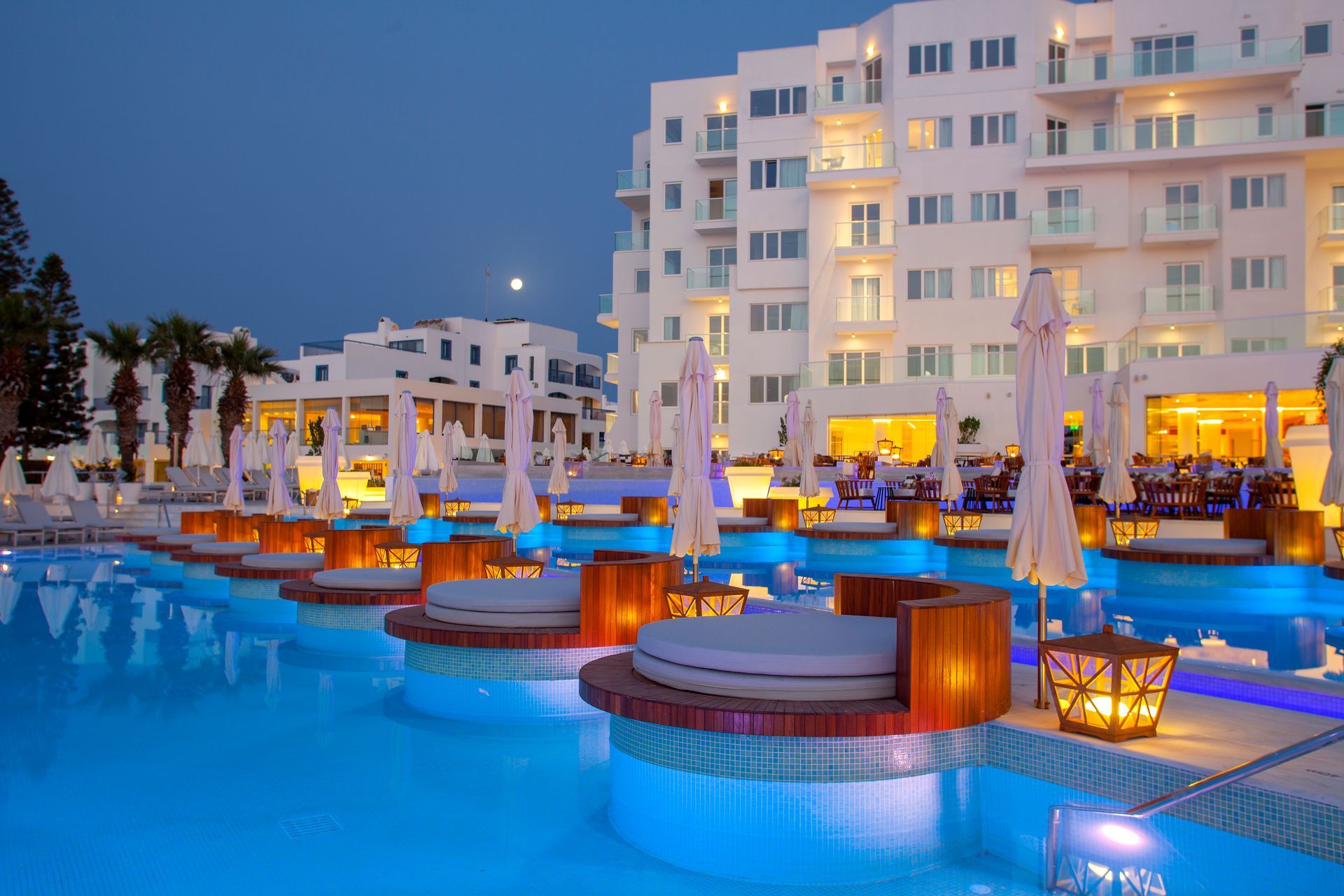 Poolside resort at night with lit cabanas and a white building.