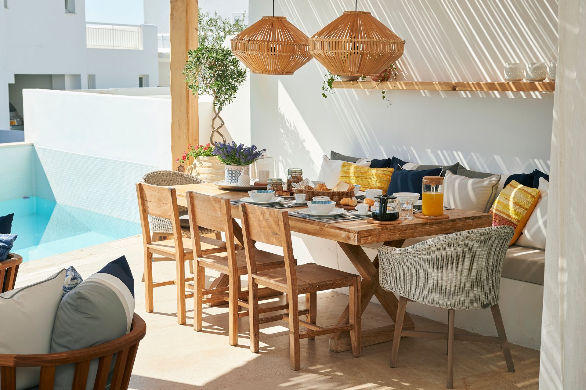 Outdoor dining area with wooden table, chairs, pool view, and hanging woven lamps.