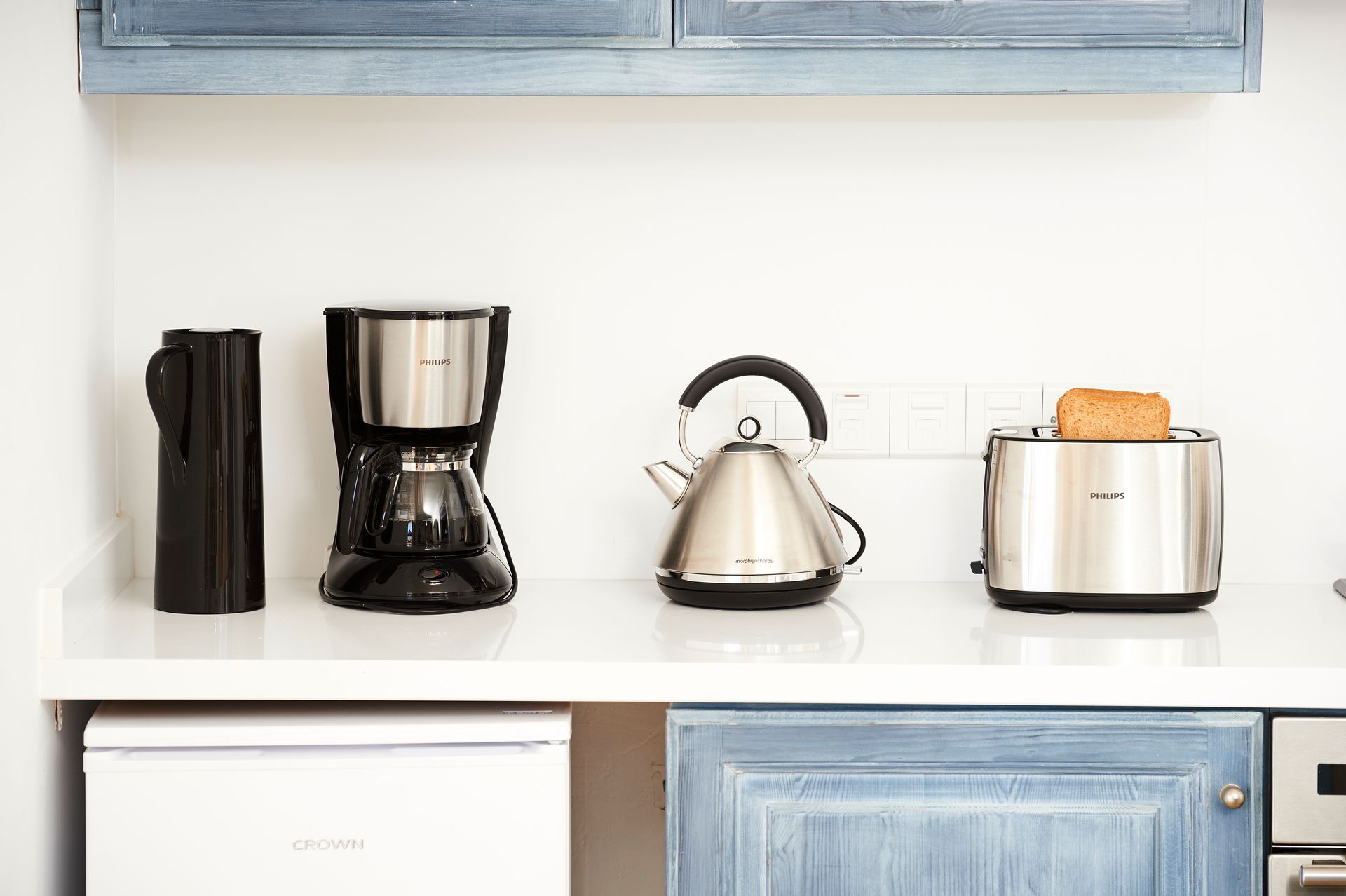 Kitchen countertop with appliances: thermos, coffee maker, kettle, toaster with toast.