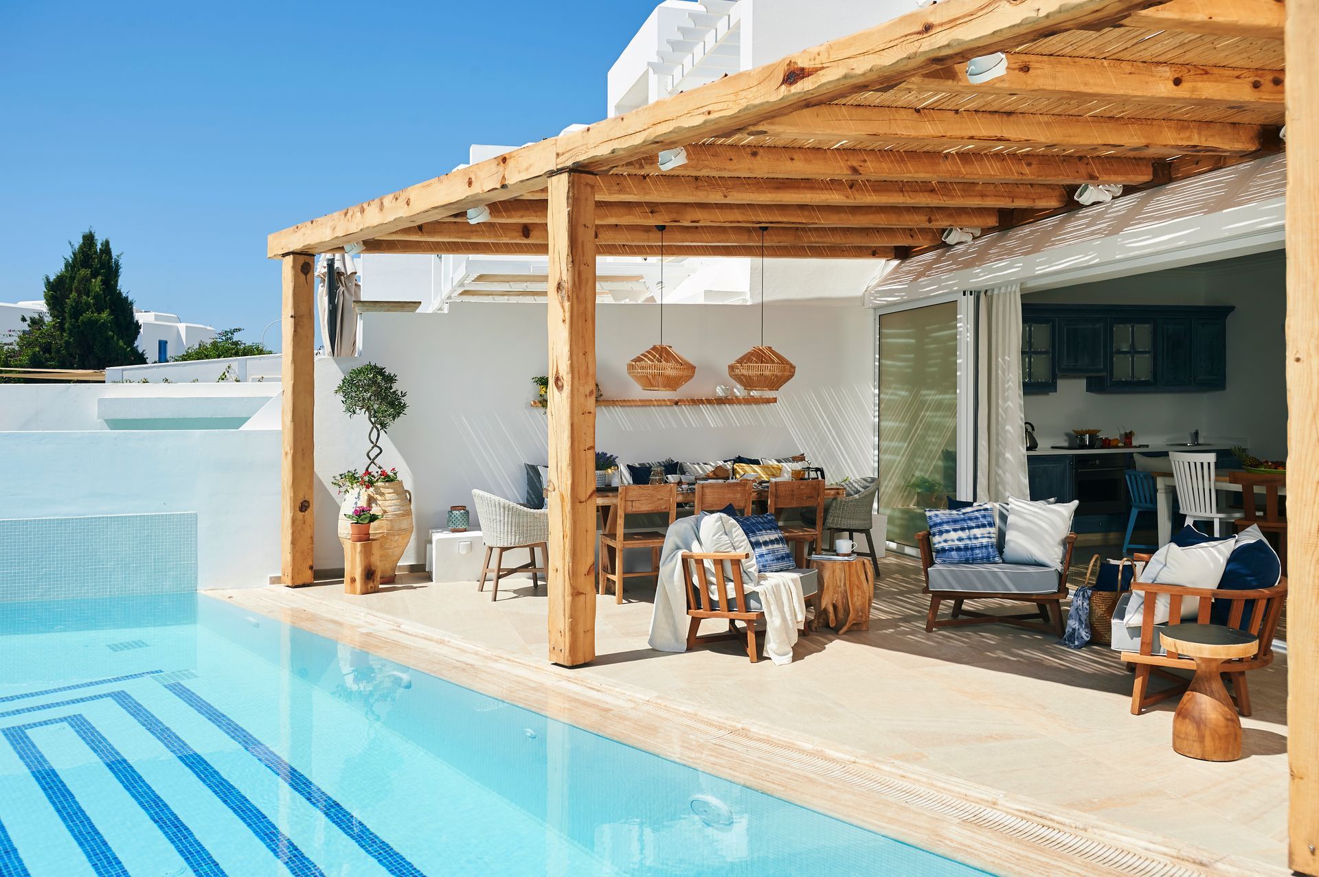 Poolside dining area with wooden pergola, table set for a meal, and blue pool.