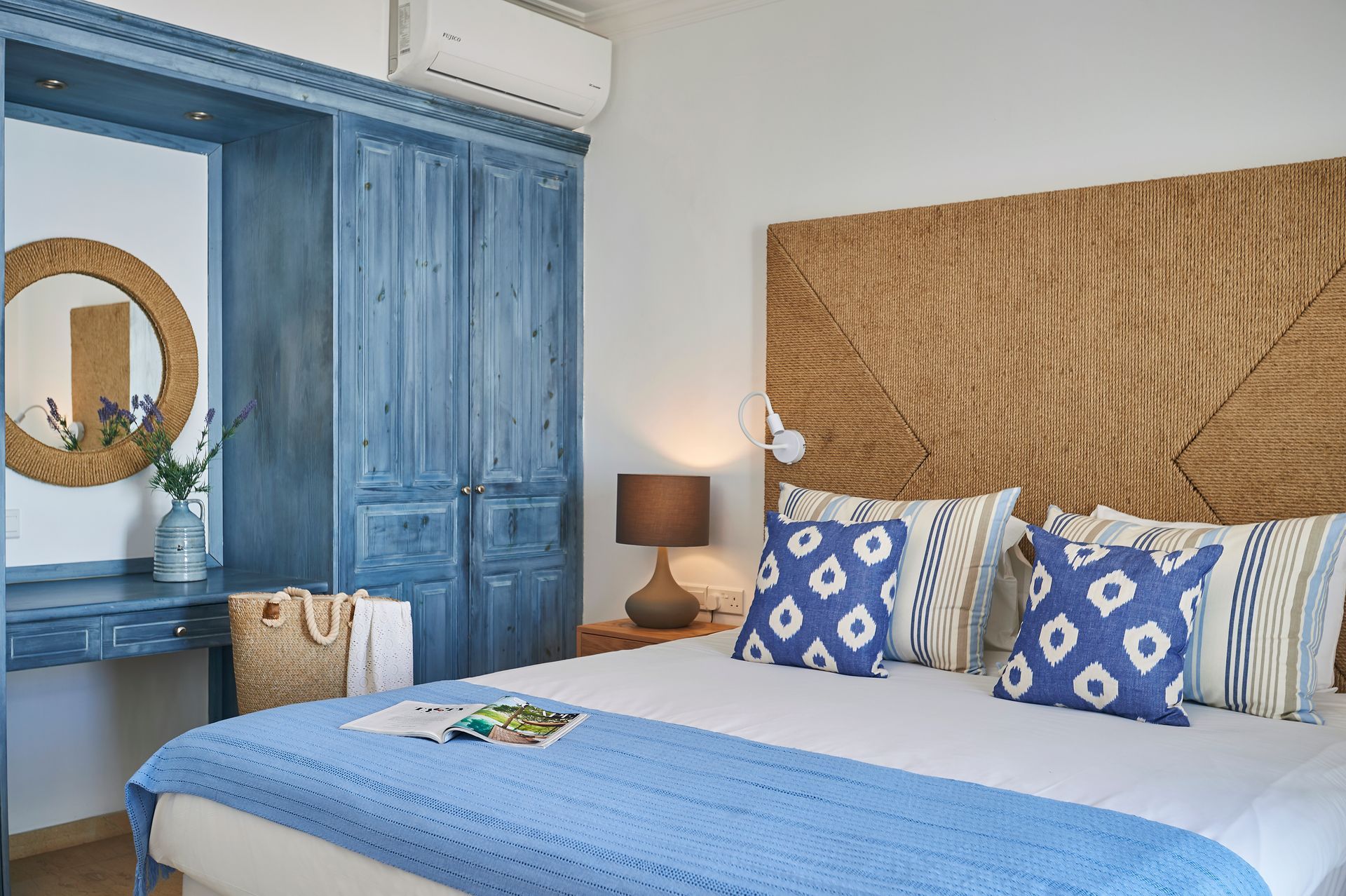 Blue-toned bedroom with bed, wicker headboard, matching blue furniture, mirror, and light blue accents.