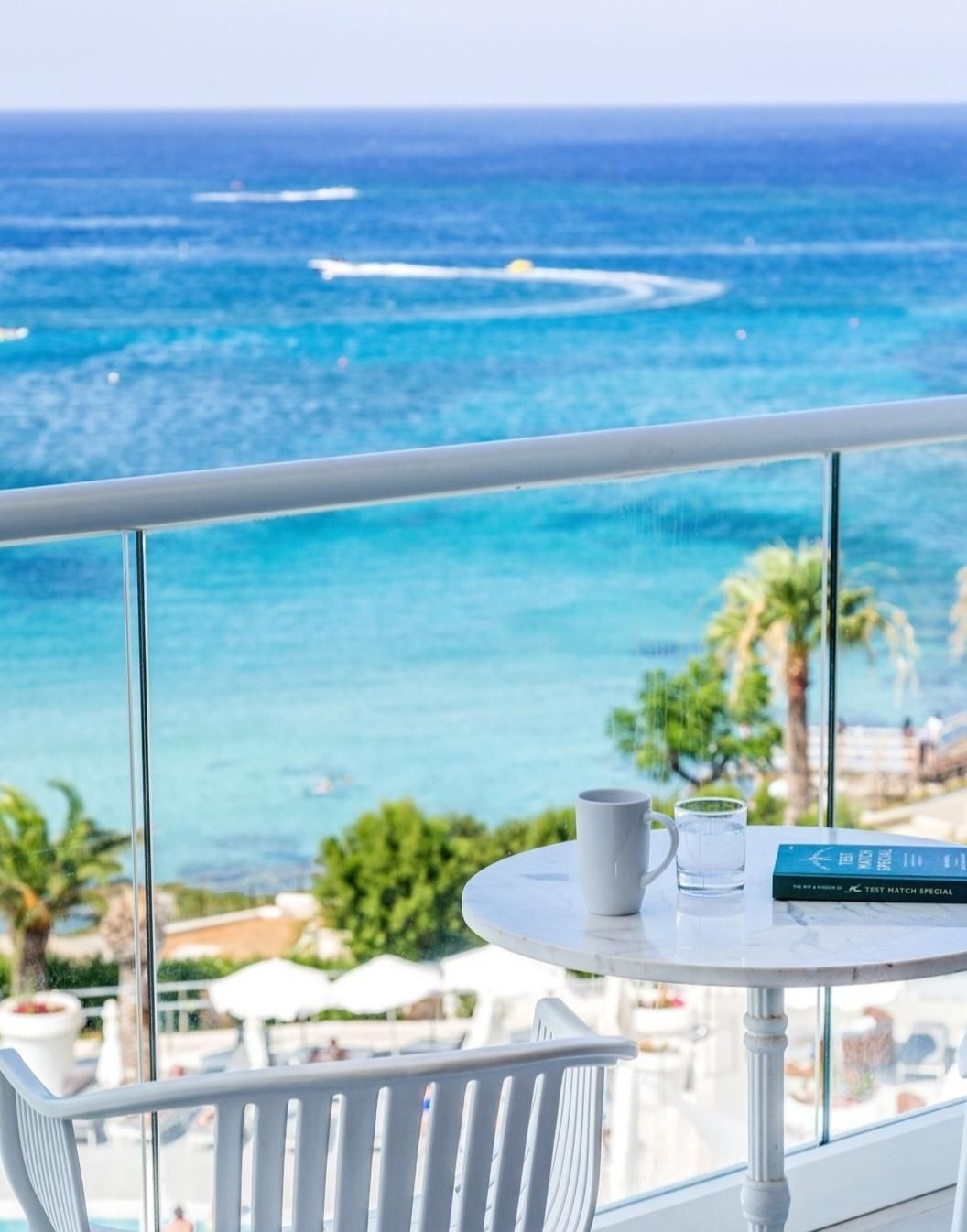 Balcony with white table, coffee cup, and book overlooking the blue sea.