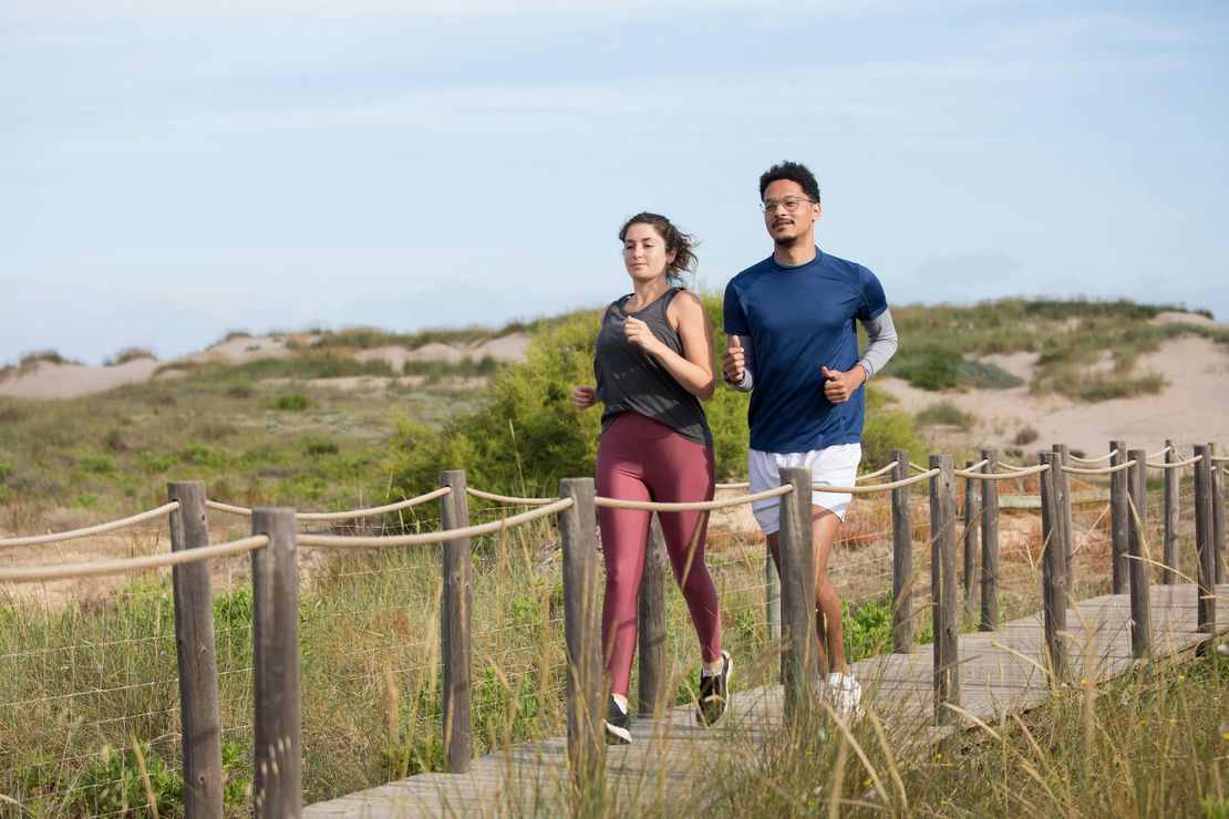 A man and a woman are running on a wooden path.