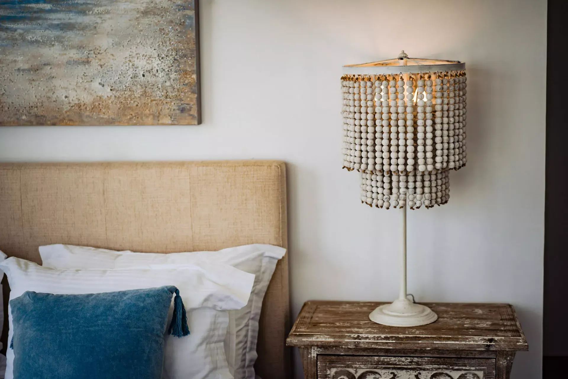 A bedroom with a bed , nightstand , lamp and painting on the wall.