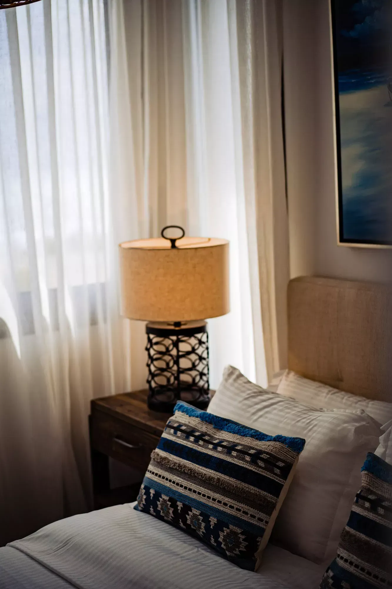A bedroom with a bed , nightstand , lamp and window.