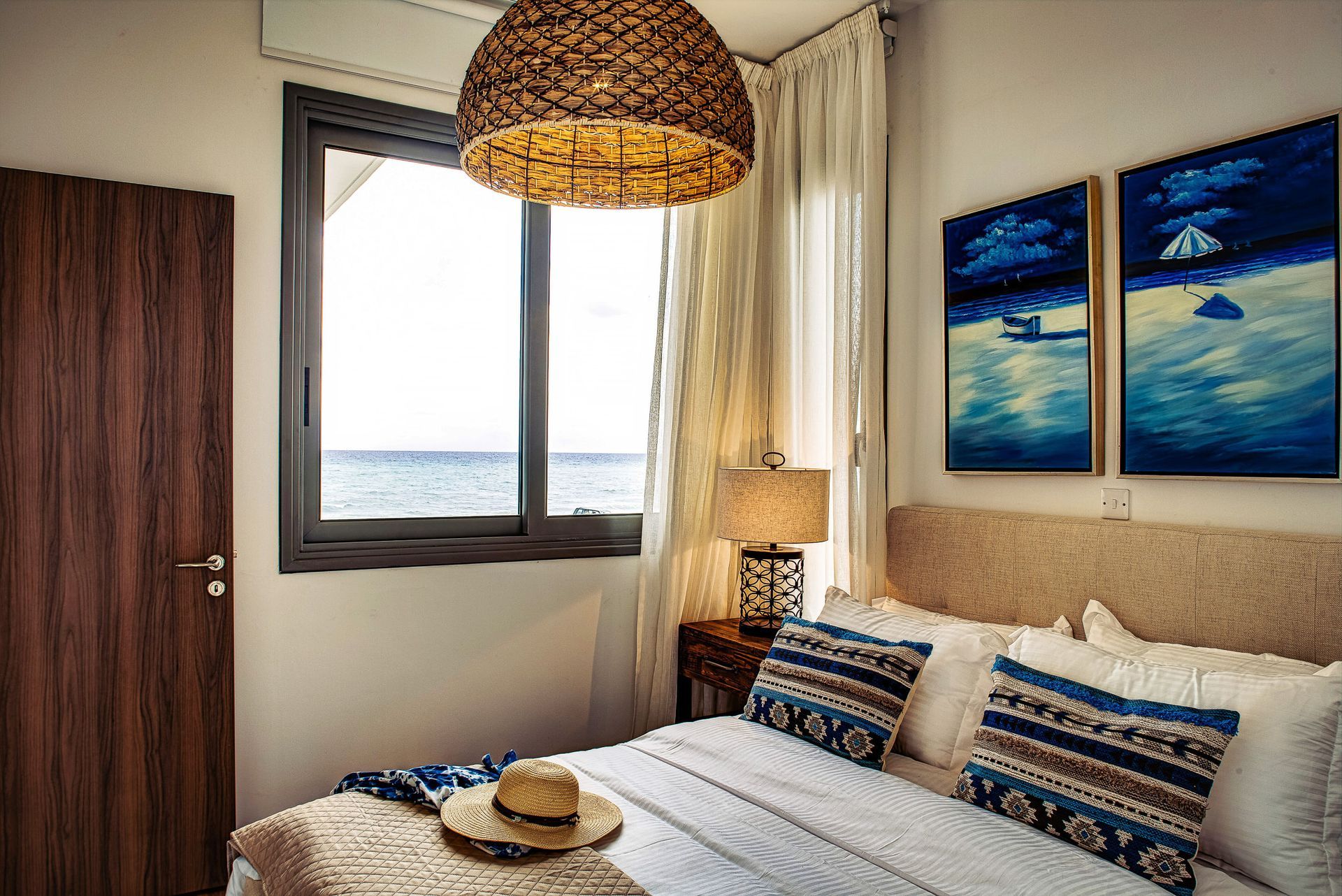 A bedroom with a bed , a window , a lamp , and two paintings on the wall.