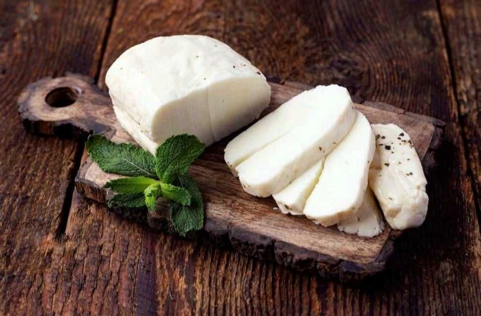 A piece of cheese is sitting on a wooden cutting board with mint leaves.