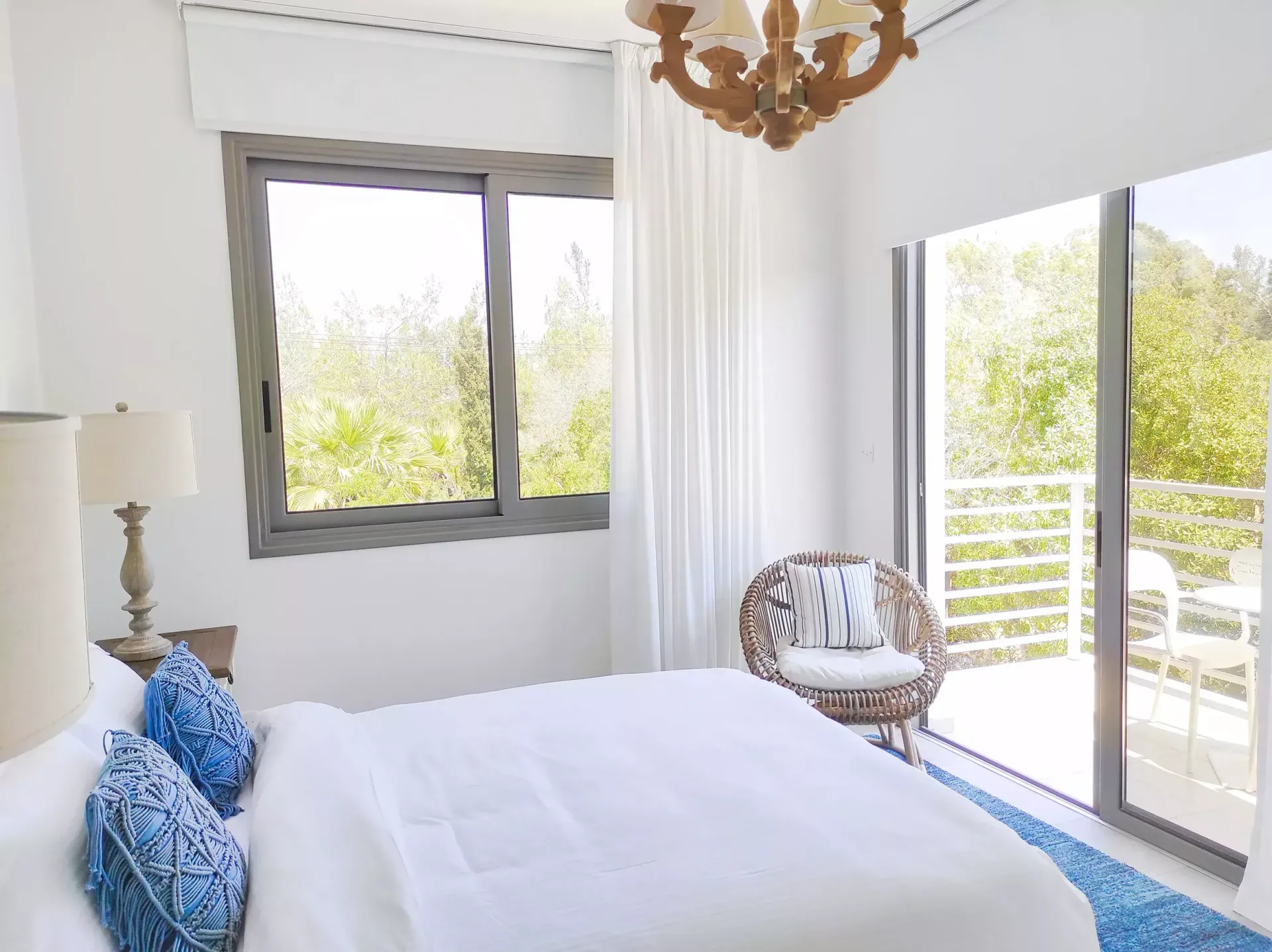 A bedroom with a bed , chair , lamp and sliding glass doors leading to a balcony.