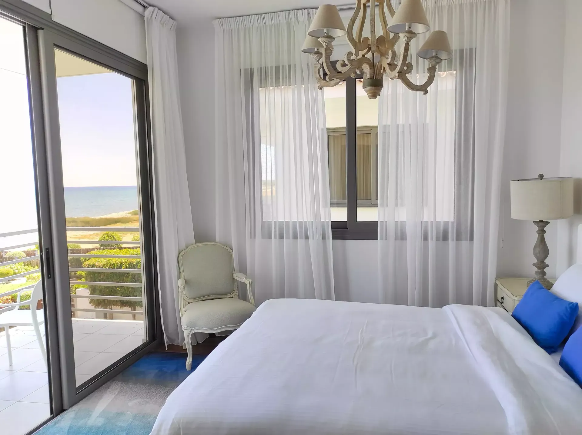 A bedroom with a king size bed , chair , lamp and sliding glass doors.