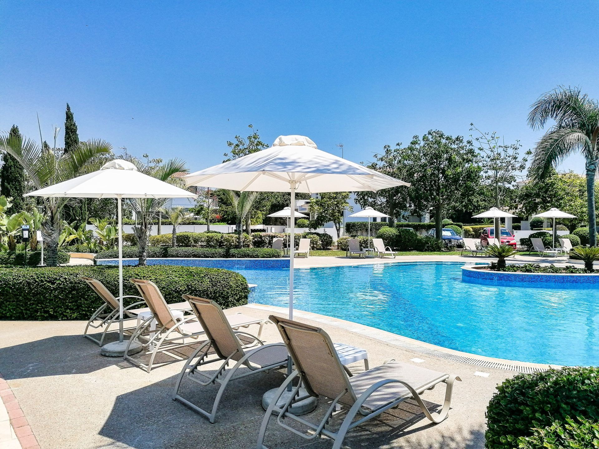 Poolside scene with lounge chairs, white umbrellas, and blue water under a sunny sky.