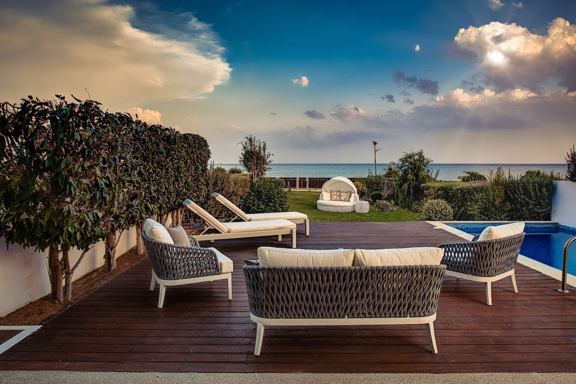 A patio with a couch , chairs and a swimming pool with a view of the ocean.