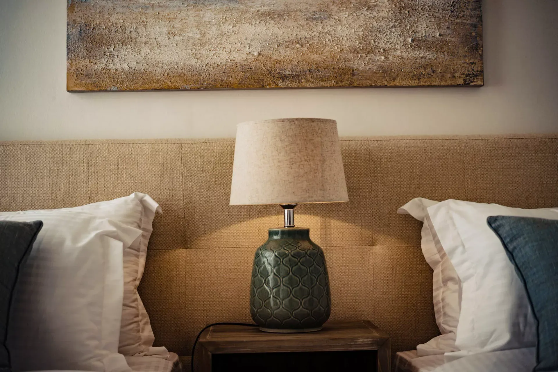 A bedroom with two beds and a lamp on a nightstand.