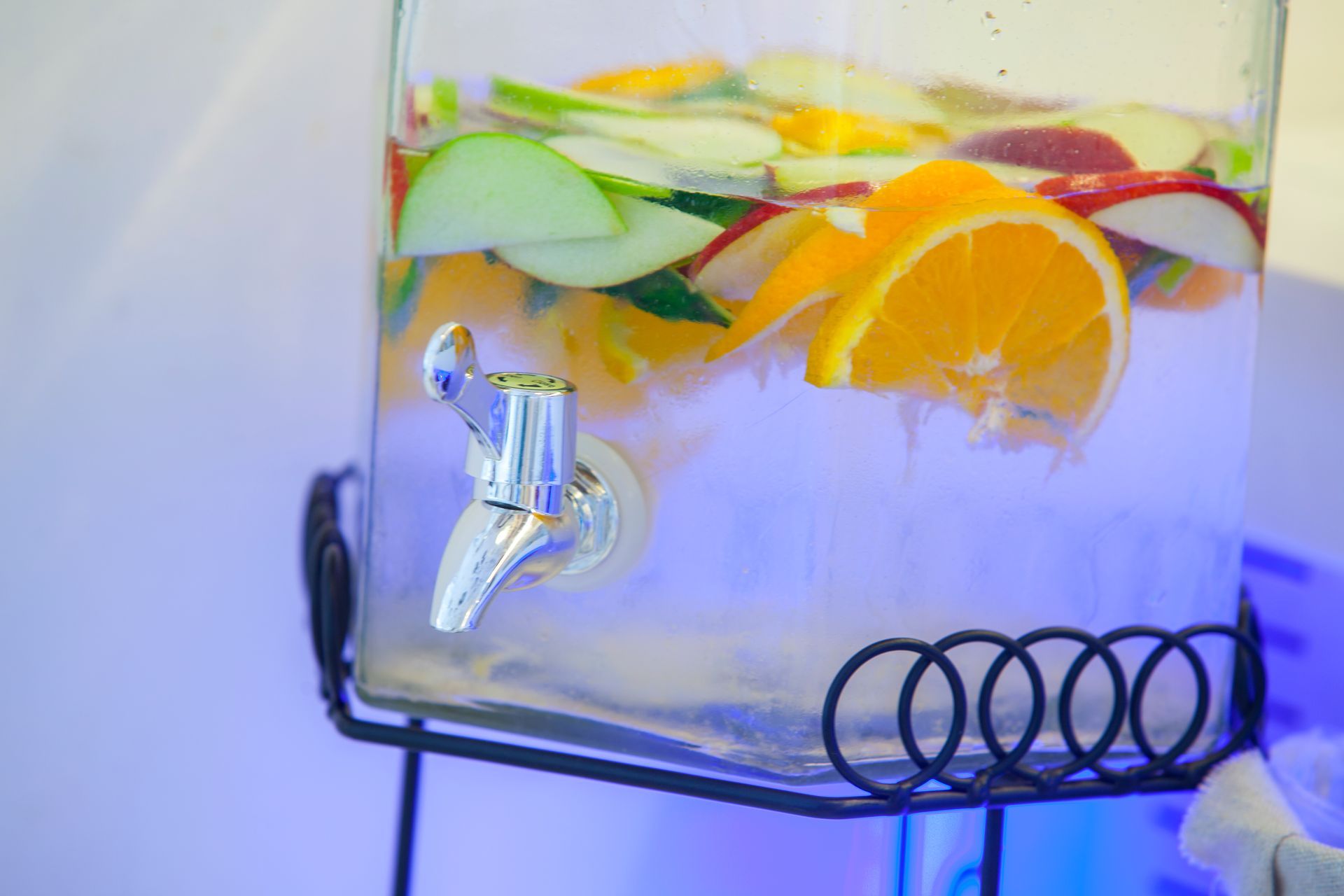 Water dispenser filled with water and sliced oranges and apples.