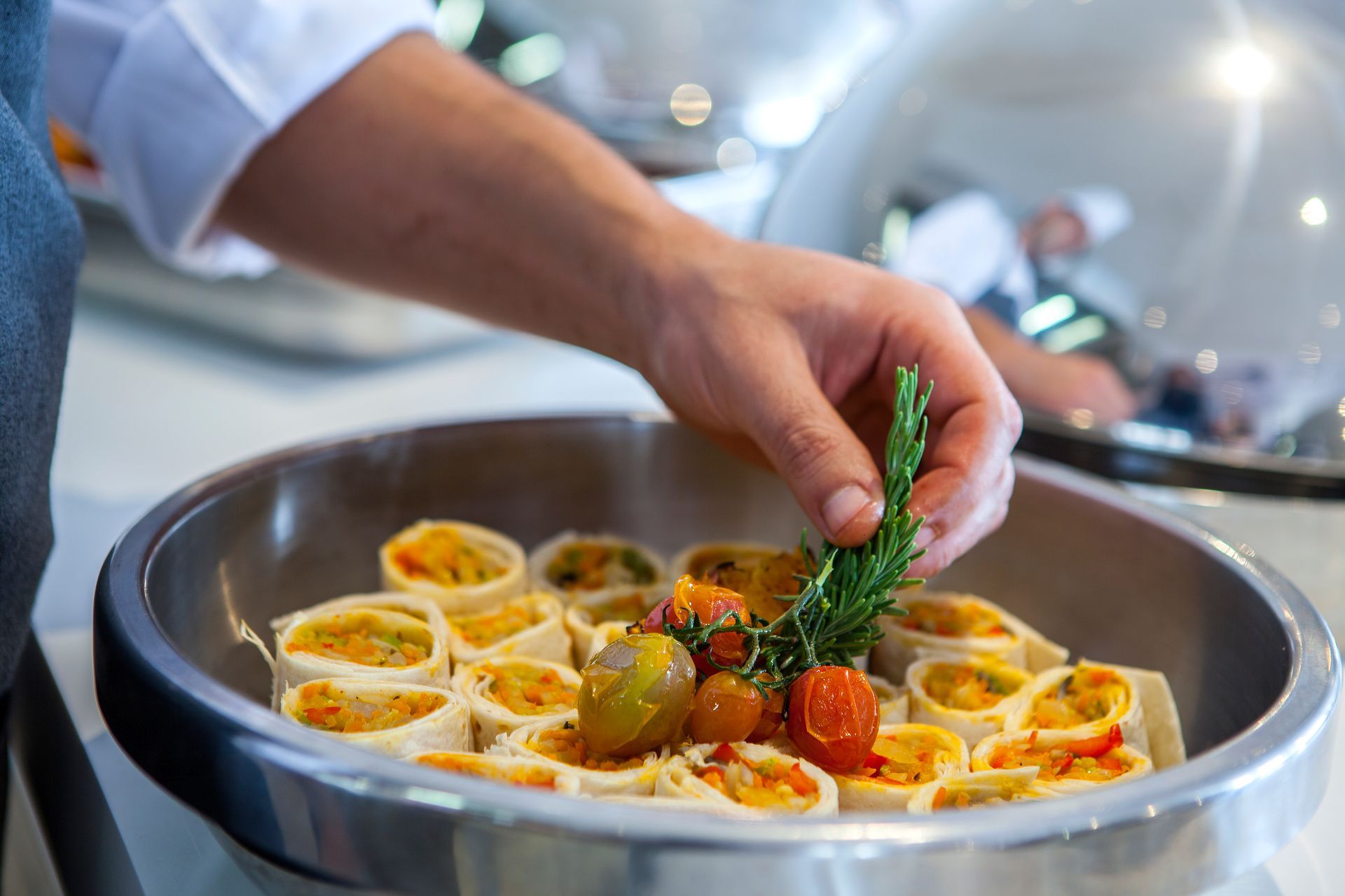 Chef garnishing wrapped food with herbs and tomatoes in a metal serving dish at King Jason Protaras.