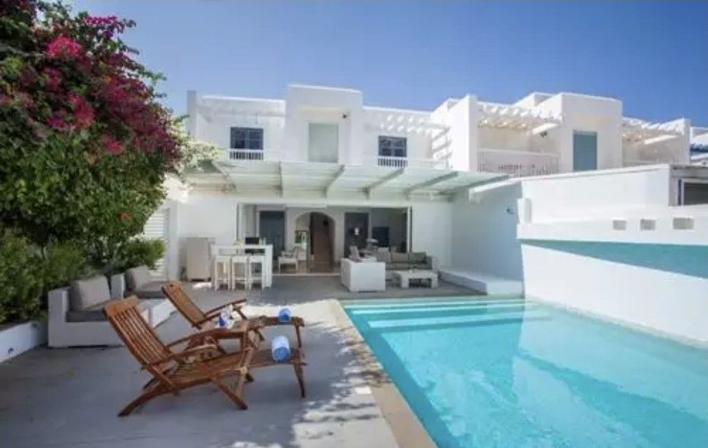 White villa with a pool, two lounge chairs, and bougainvillea on a sunny day.